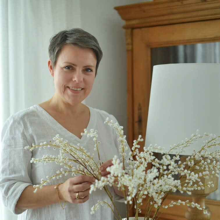 Frau in weißer Bluse hält dekorative Zweige mit weißen Blüten in hellem Raum