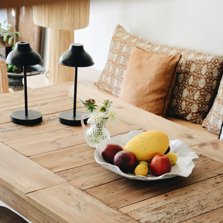 Holztisch mit dekorativer weißer Obstschale und zwei schwarzen Tischlampen in gemütlichem Raum