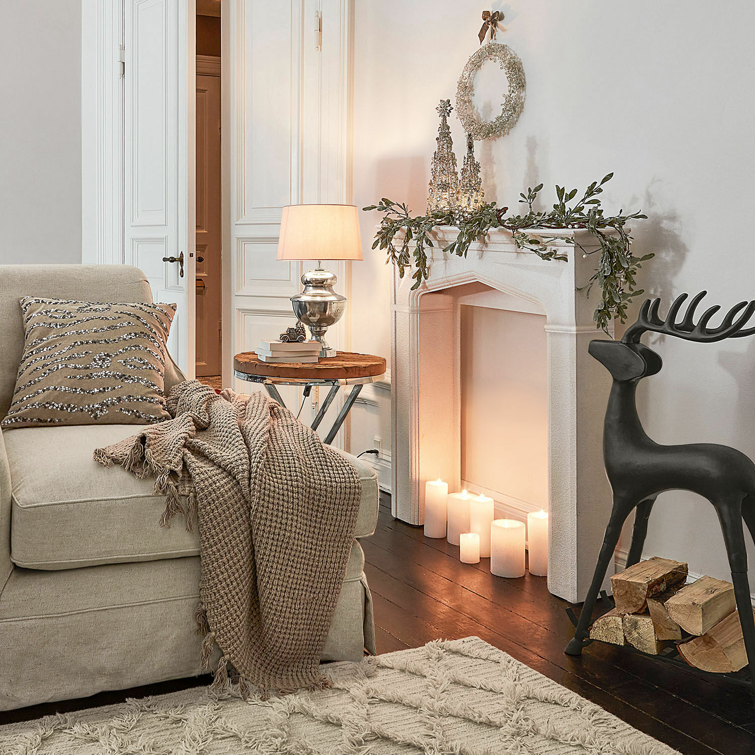 Gemütliches Wohnzimmer mit beigem Sofa, brauner Decke, dekorativem Kissen und Kamin mit weißen Kerzen