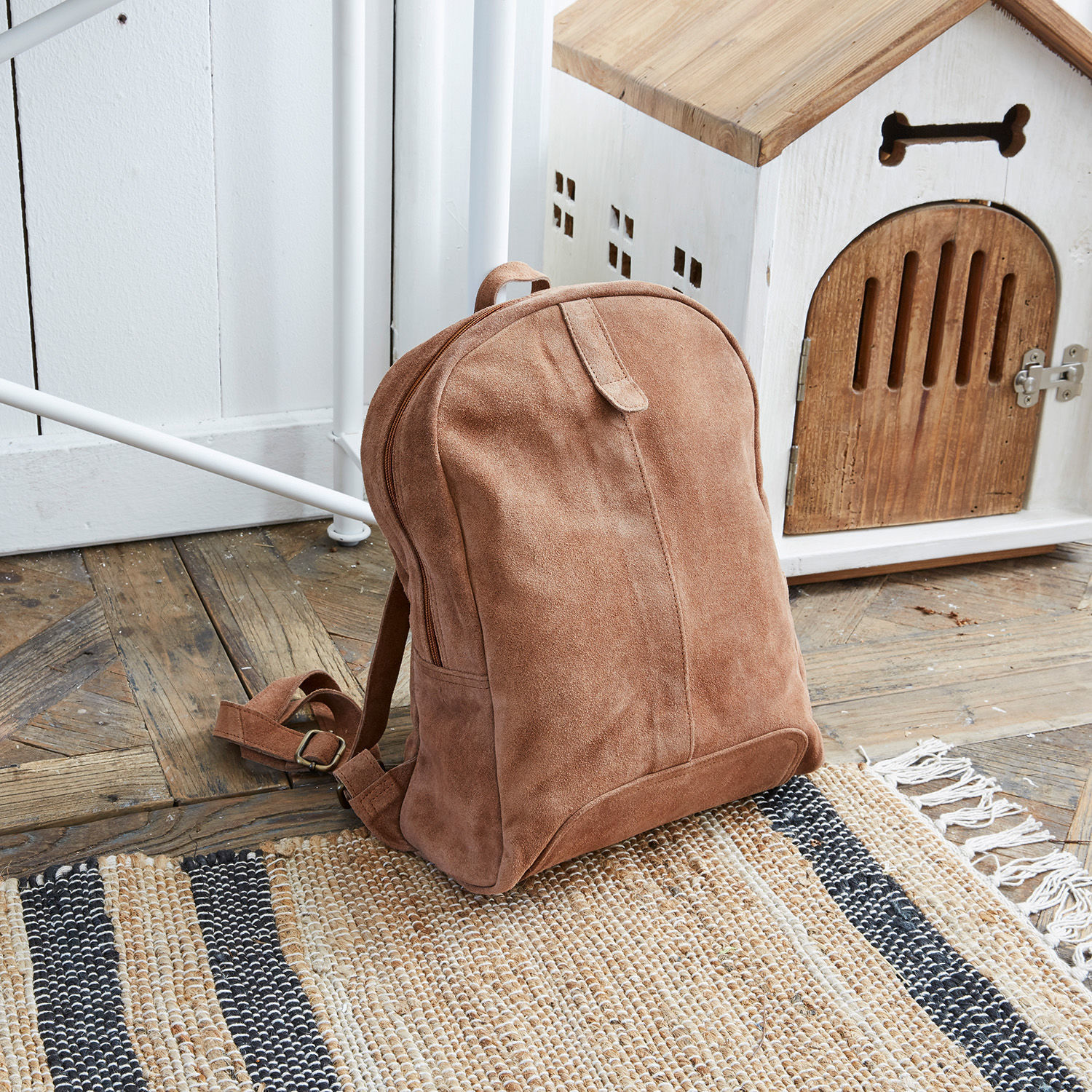 Rucksack Palau Brauner Wildleder-Rucksack auf Holzboden neben weißem Hundehäuschen aus Holz