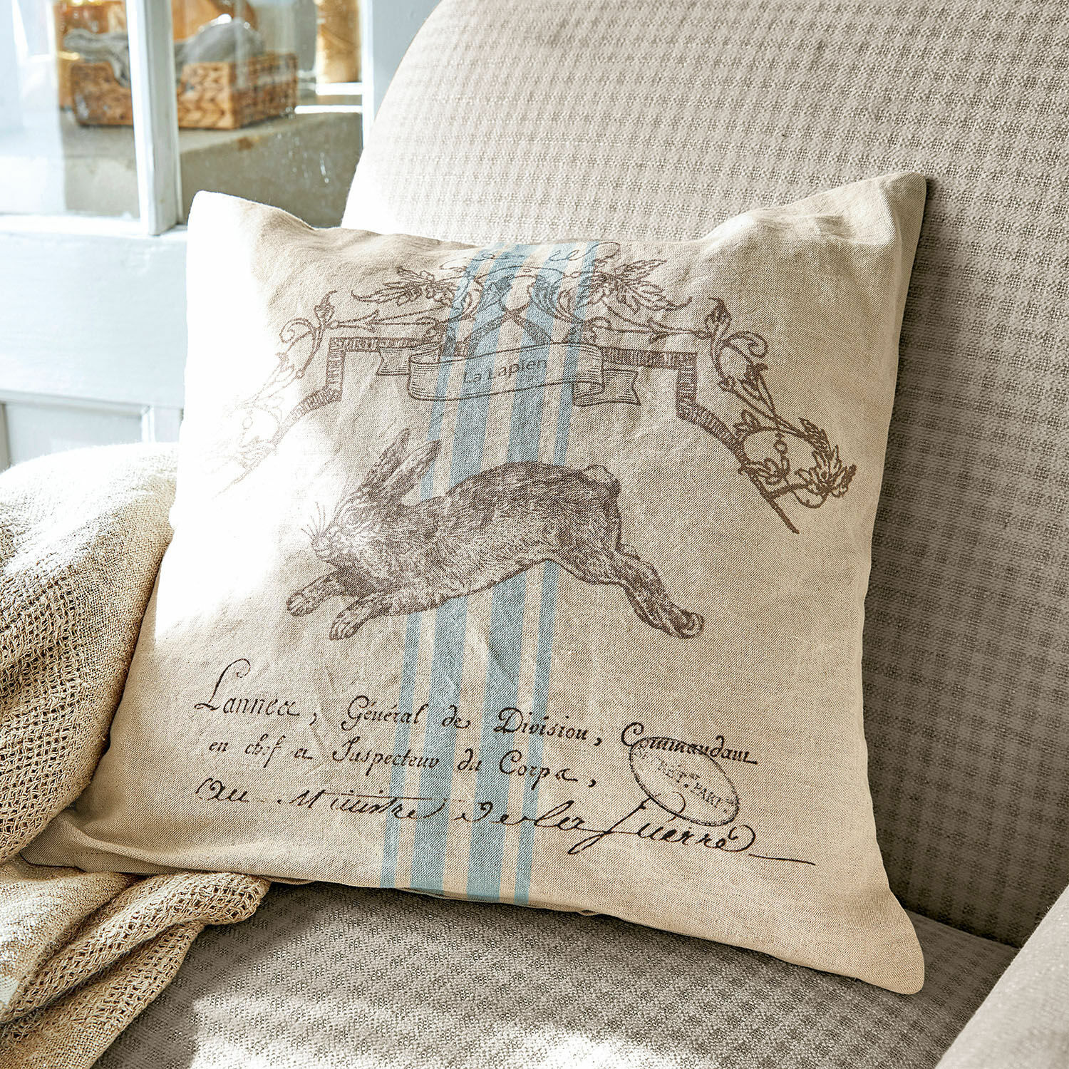 Kissenhülle La Lapin Beige Leinenkissen mit Hasenmotiv und blauen Streifen auf grauem Sofa, Wohnaccessoire