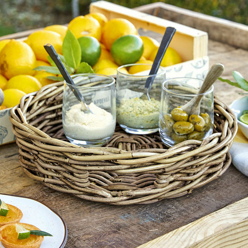 Runder Korb aus Weide mit drei Gläsern und Löffeln auf Holztisch mit Zitrusfrüchten
