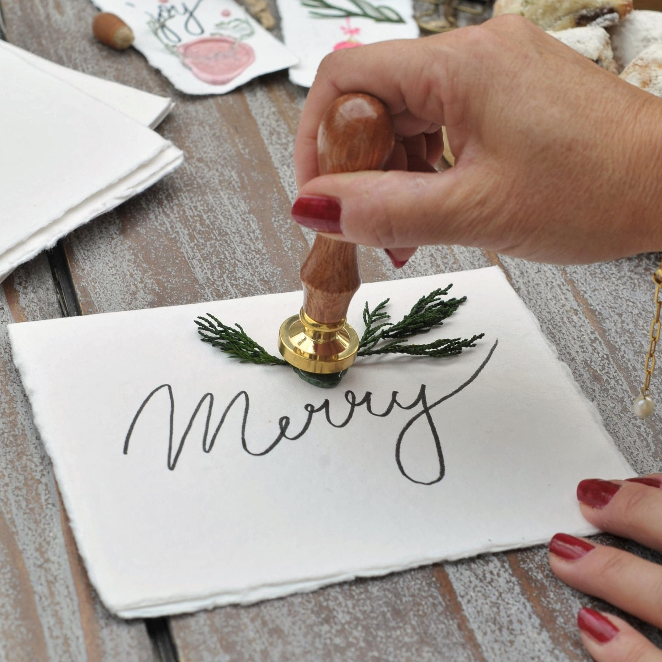 Holzstempel zum Verzieren von Geschenken auf weißer Karte mit Schriftzug Merry und grünen Zweigen