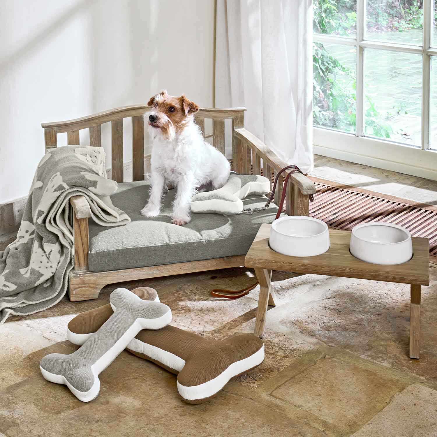 Holz-Hundebett mit grauem Kissen, Plüschknochen und weißen Futternäpfen auf Holzständer im Raum
