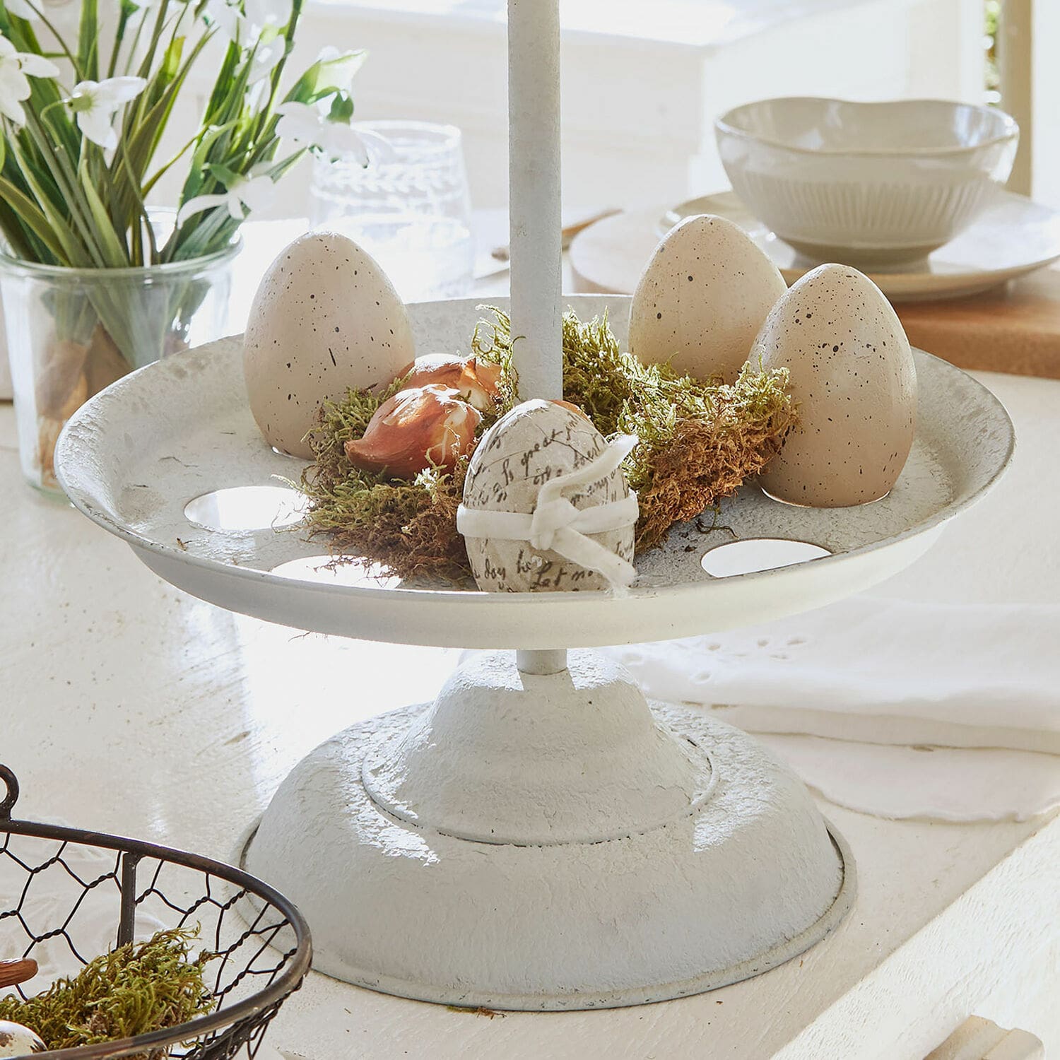 Weiße Metall-Etagere mit beigen Dekoeiern und Moos für frühlingshafte Tischdekoration
