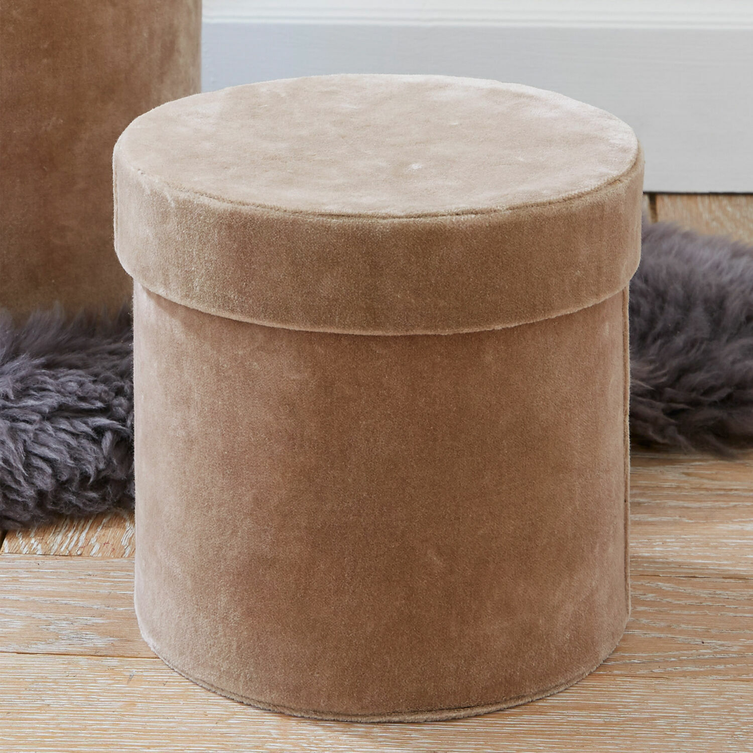 Beige runde Samtbox auf Holzboden mit grauem Fellteppich im Hintergrund