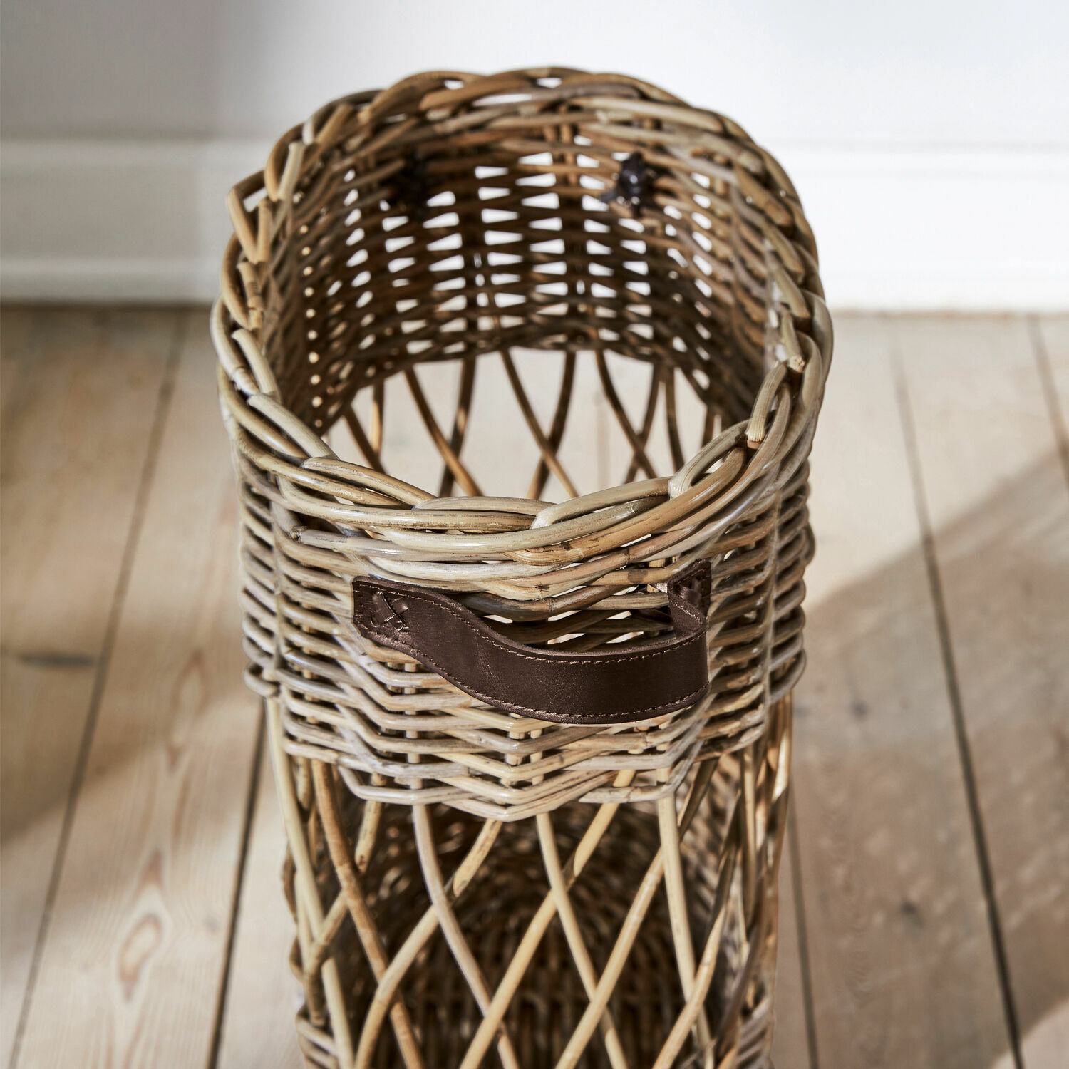 Wickerkorb mit braunem Ledergriff auf Holzboden, natürlicher Aufbewahrungskorb aus Rattan