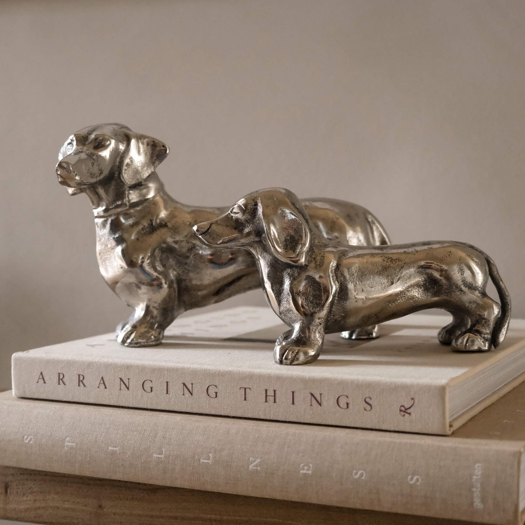 Zwei silberne Dackel-Figuren aus Metall auf einem Bücherstapel als Wohnaccessoire