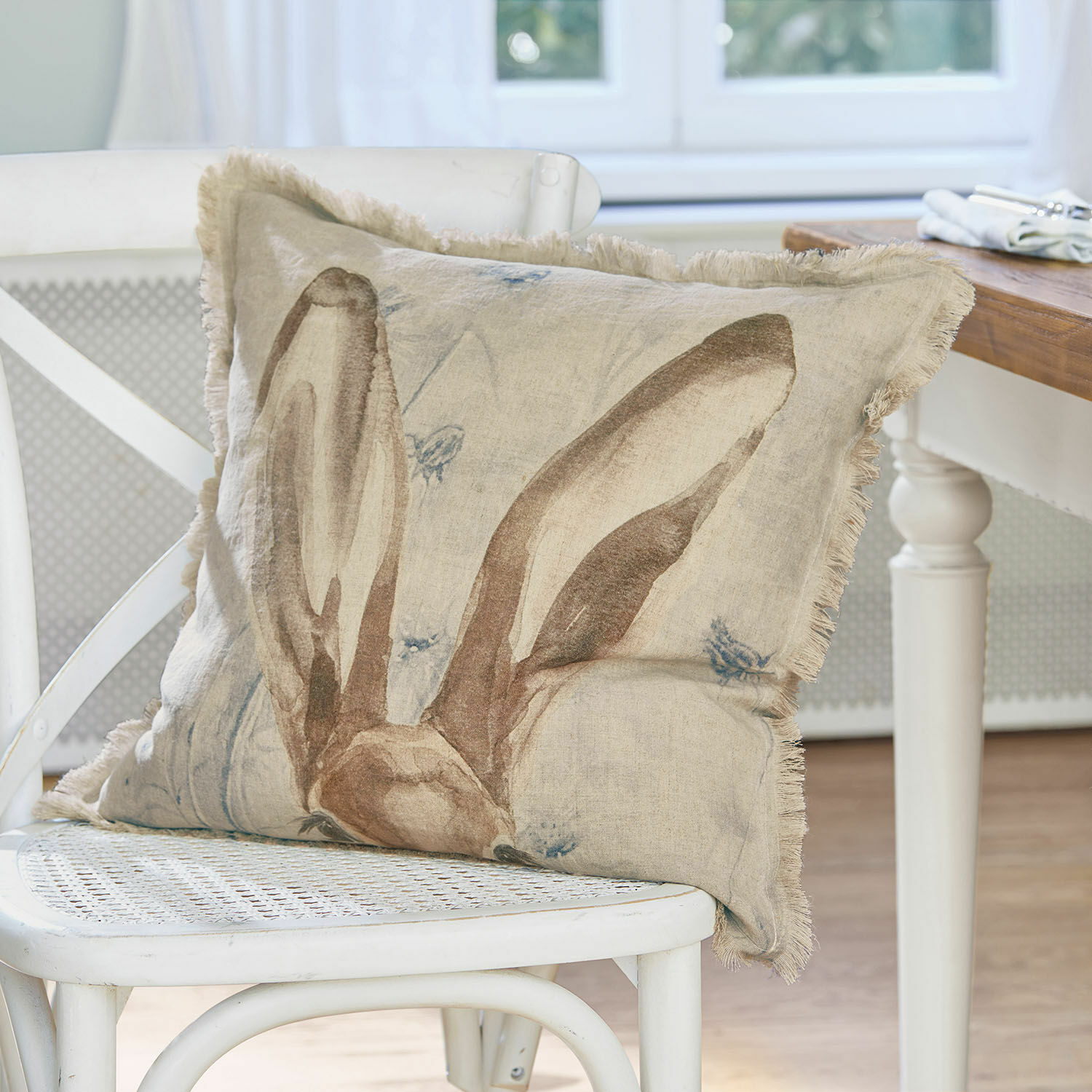 Kissenhülle Kameron Beige Leinenkissen mit Hasenohren-Motiv auf weißem Stuhl als Wohnaccessoire
