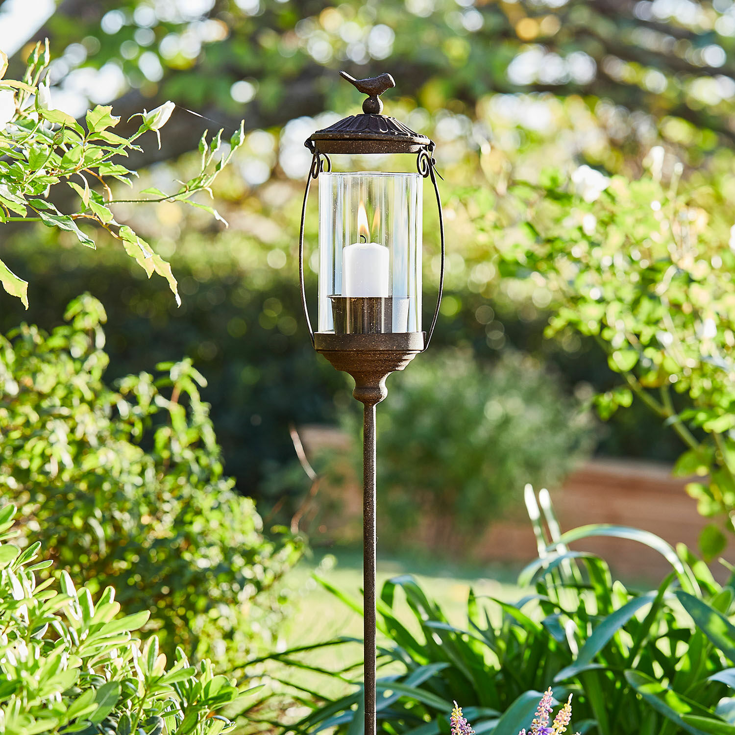 Laterne Nexoril Metall-Gartenlaterne mit weißer Kerze und Glaszylinder vor grünem Pflanzenhintergrund