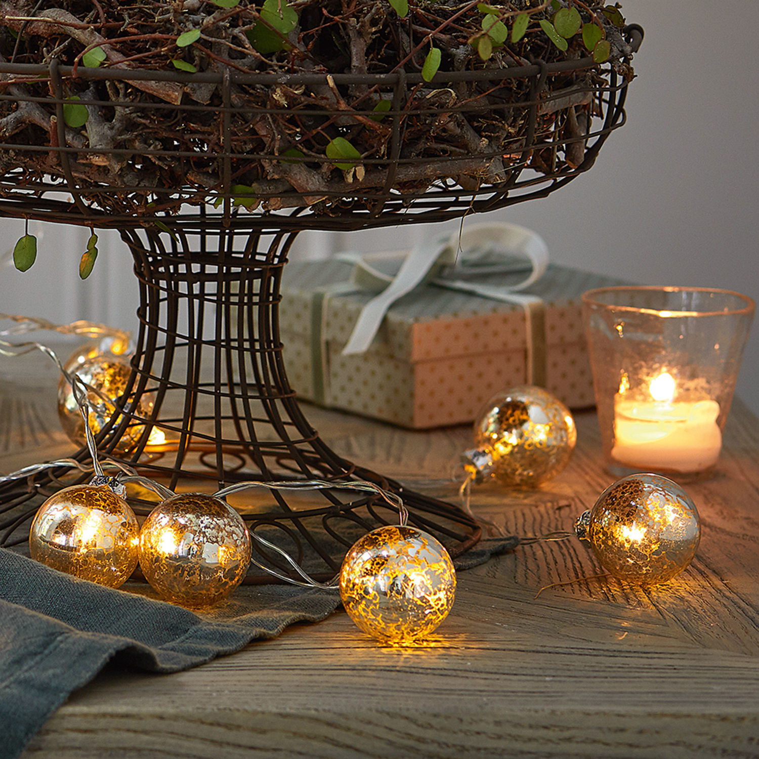 Dekorative goldene Glas-Lichterkette auf Holztisch mit Geschenk und brennender Kerze