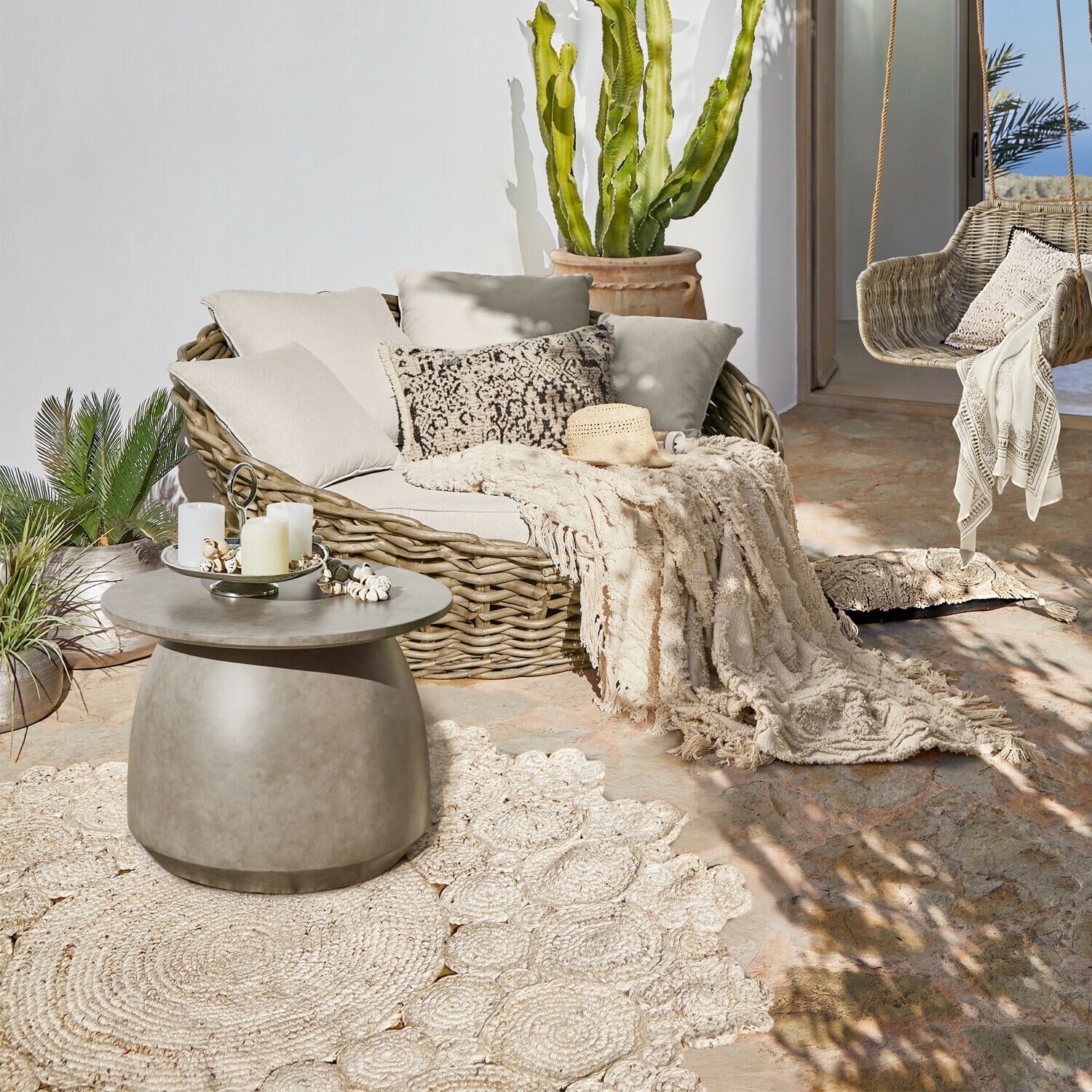 Gemütliche Rattanmöbel mit beigen Kissen und grauem Beistelltisch auf sonniger Terrasse