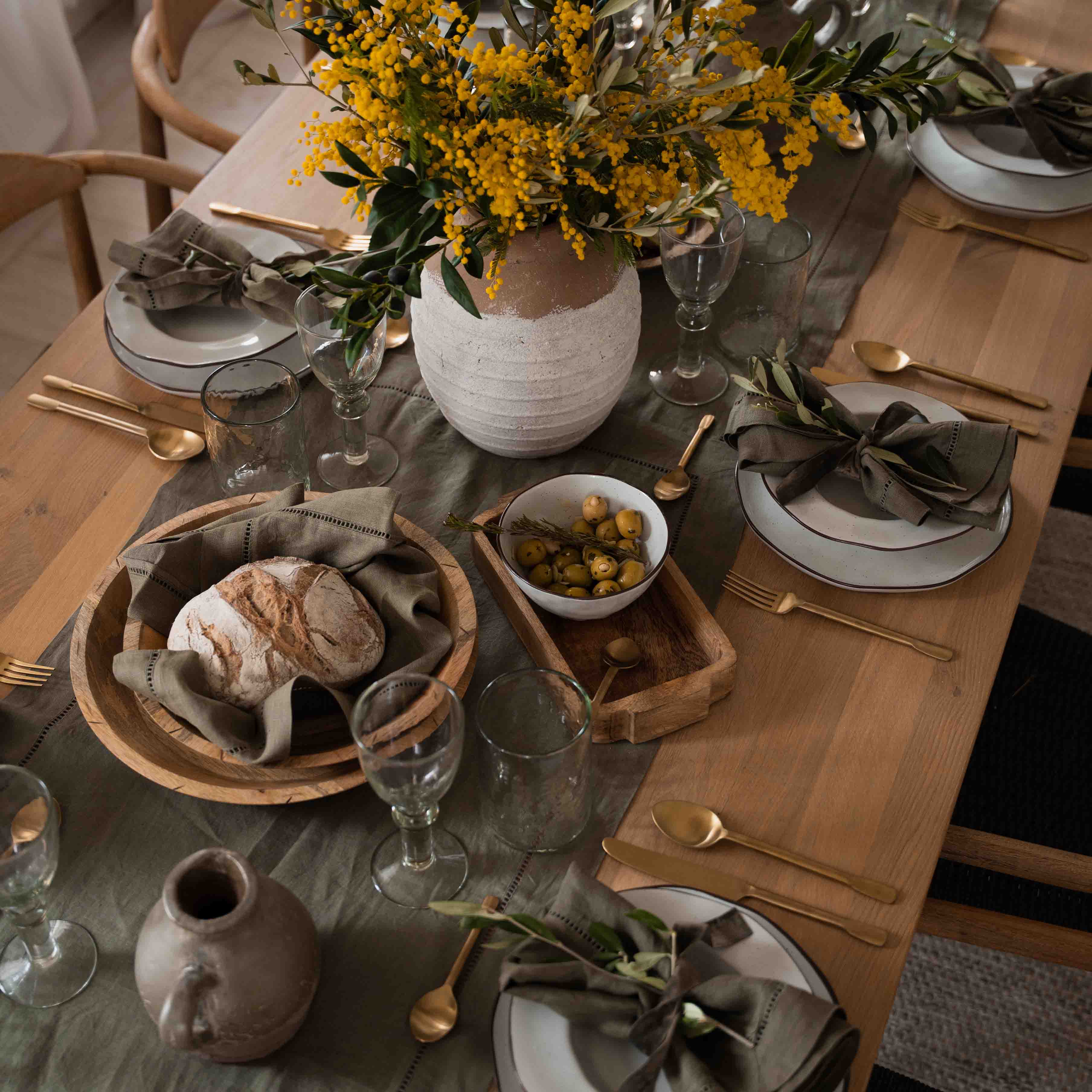 Rustikaler Holztisch mit weißem Geschirr, grünen Servietten und gelbem Blumenstrauß in Tonvase