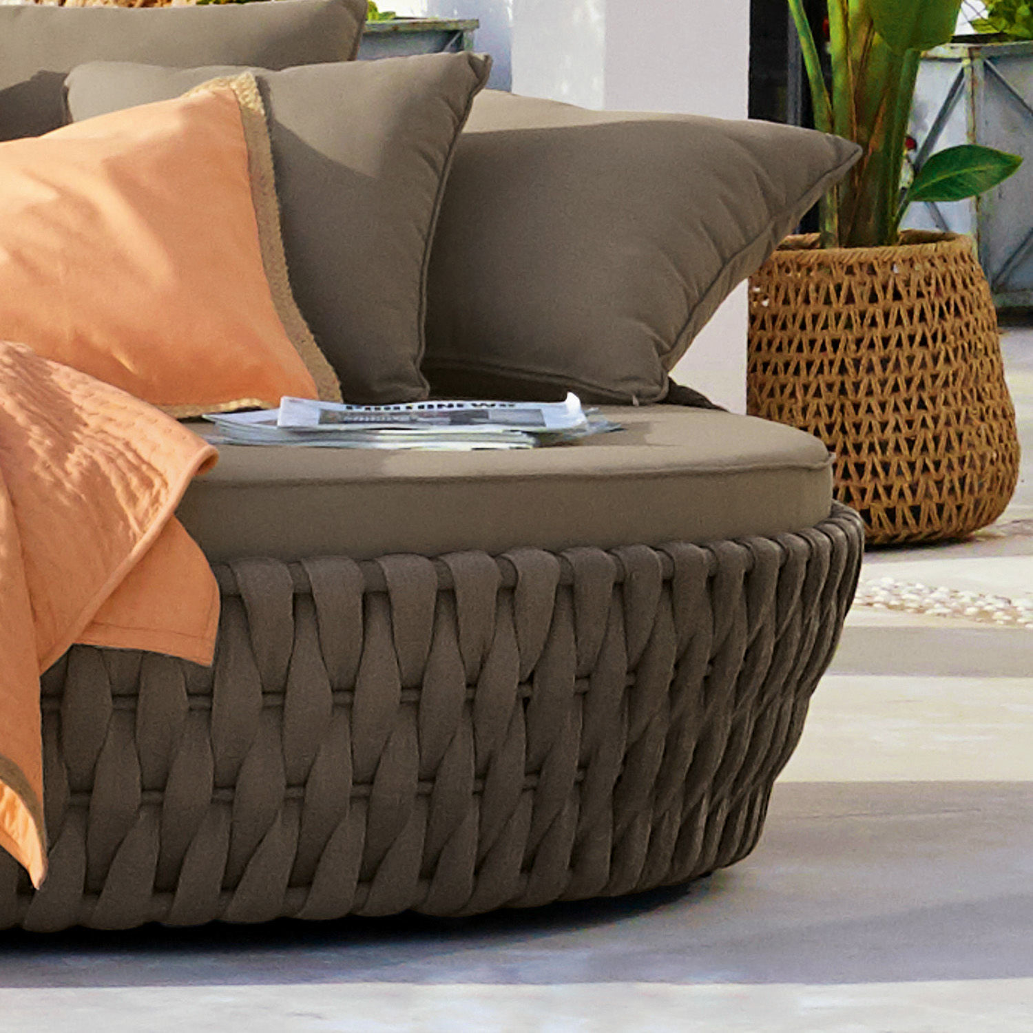 Braunes, geflochtenes Sofa mit weichen Kissen und orangefarbener Decke für Terrasse oder Garten
