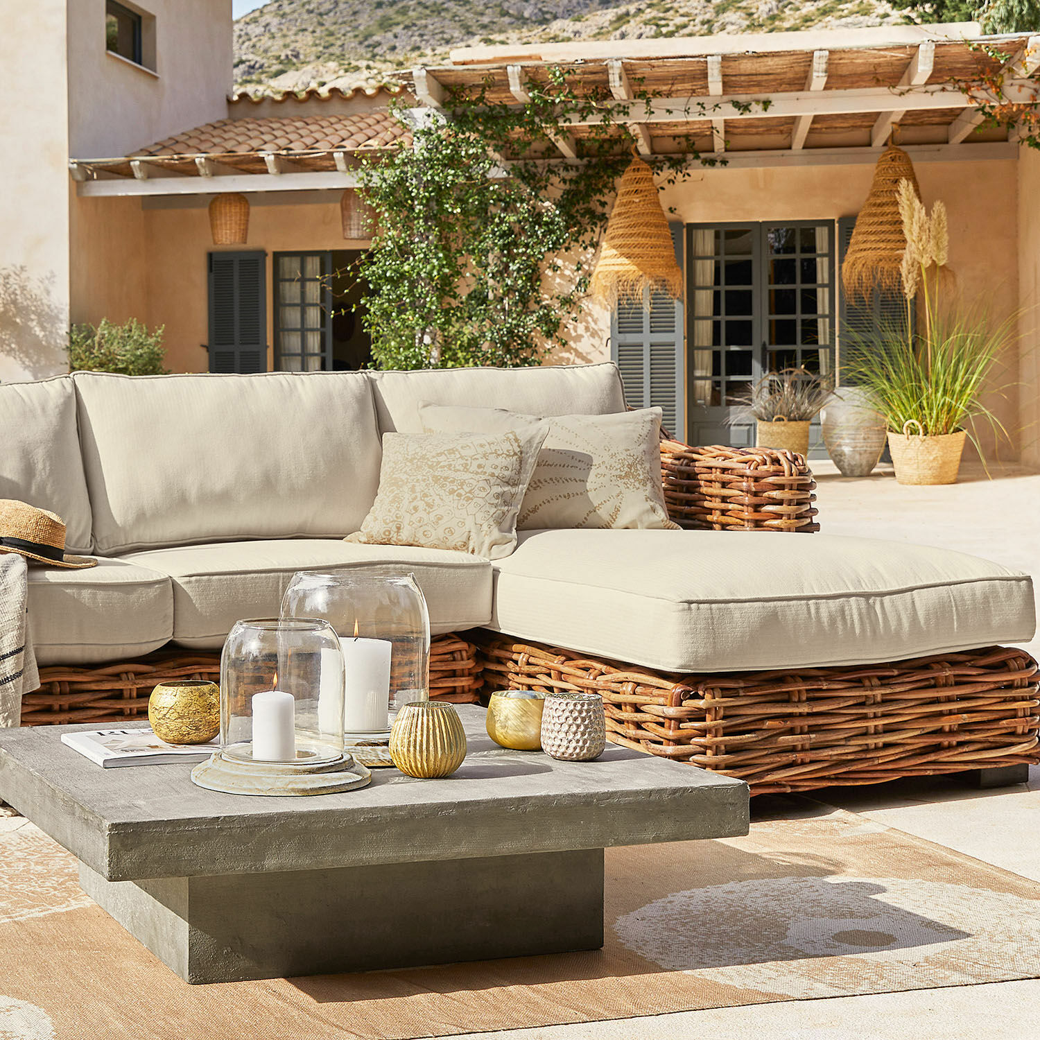 Outdoor-Sitzgruppe mit beigen Polstern und Rattanrahmen, quadratischer Beton-Couchtisch auf sonniger Terrasse