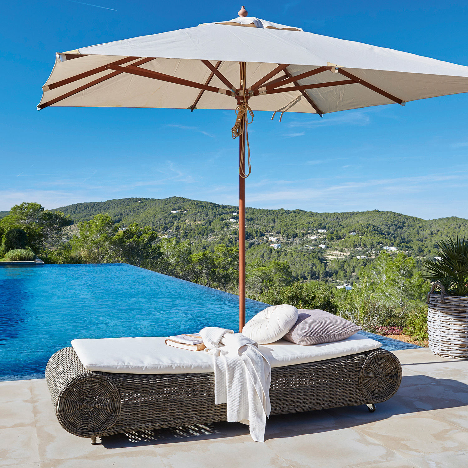 Graue Rattan-Liege mit weißer Polsterung und Sonnenschirm neben Infinity-Pool