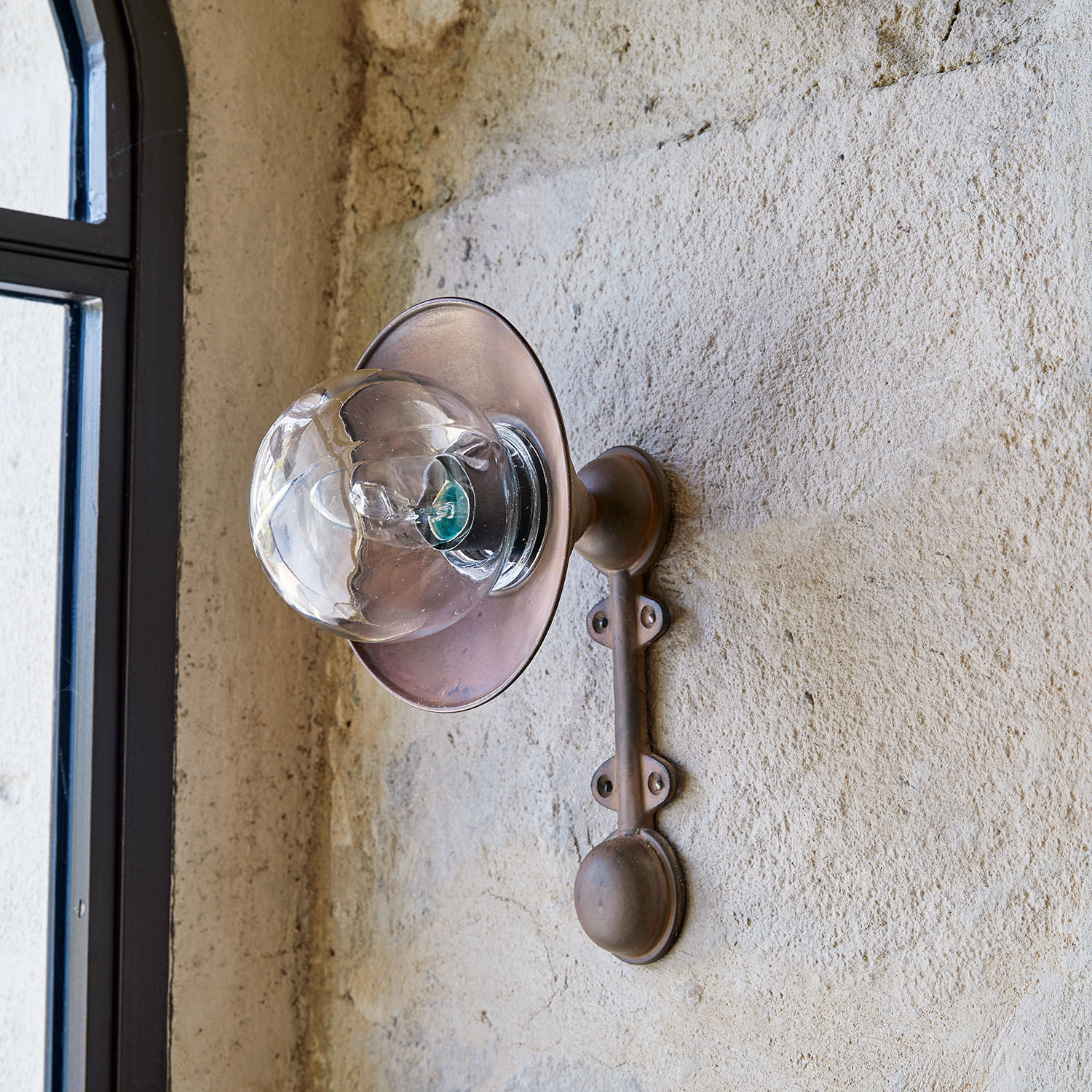 Vintage Messing-Wandleuchte mit klarem Glas-Schirm an strukturierter Putzwand montiert