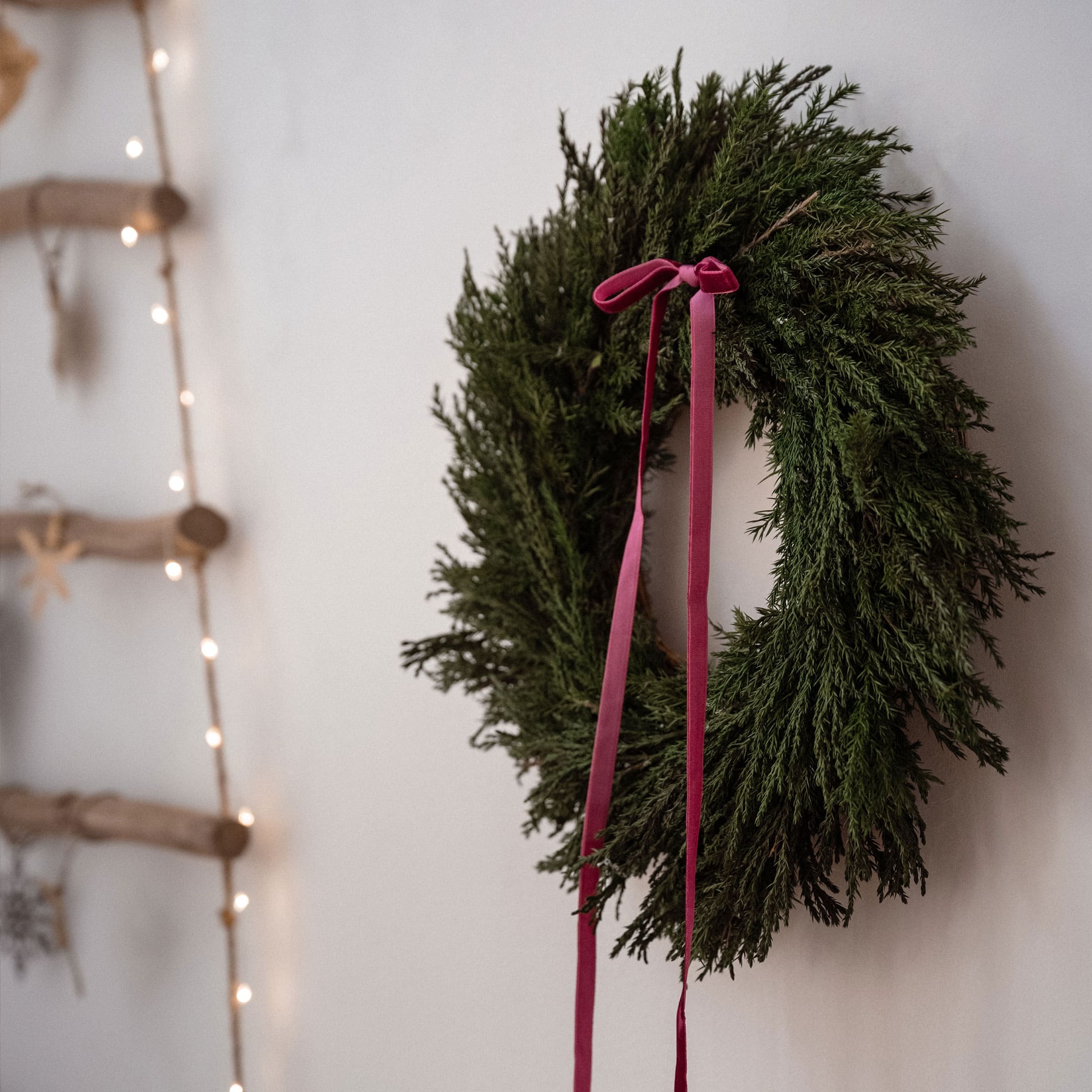 Weihnachtskranz aus grünen Zweigen mit rosa Schleife an weißer Wand, festliche Dekoration