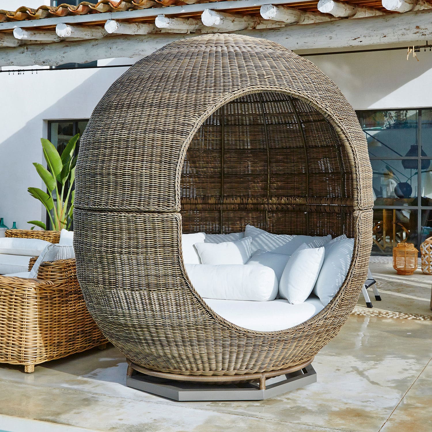Runder Korbsessel aus natürlichem Rattan mit weißen Kissen, ideal für Garten und Terrasse