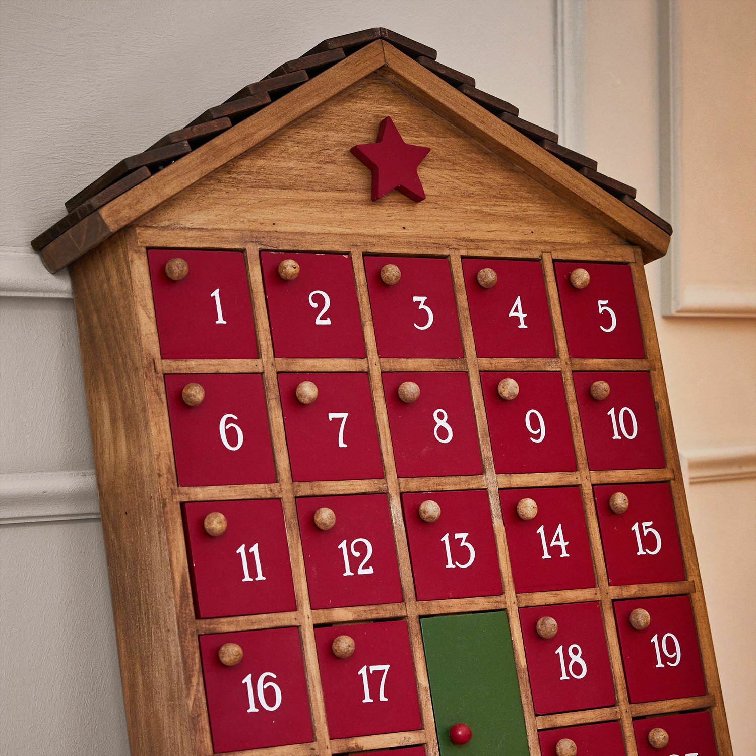 Holz-Adventskalender in Hausform mit roten und grünen Türen und rotem Stern auf dem Dach