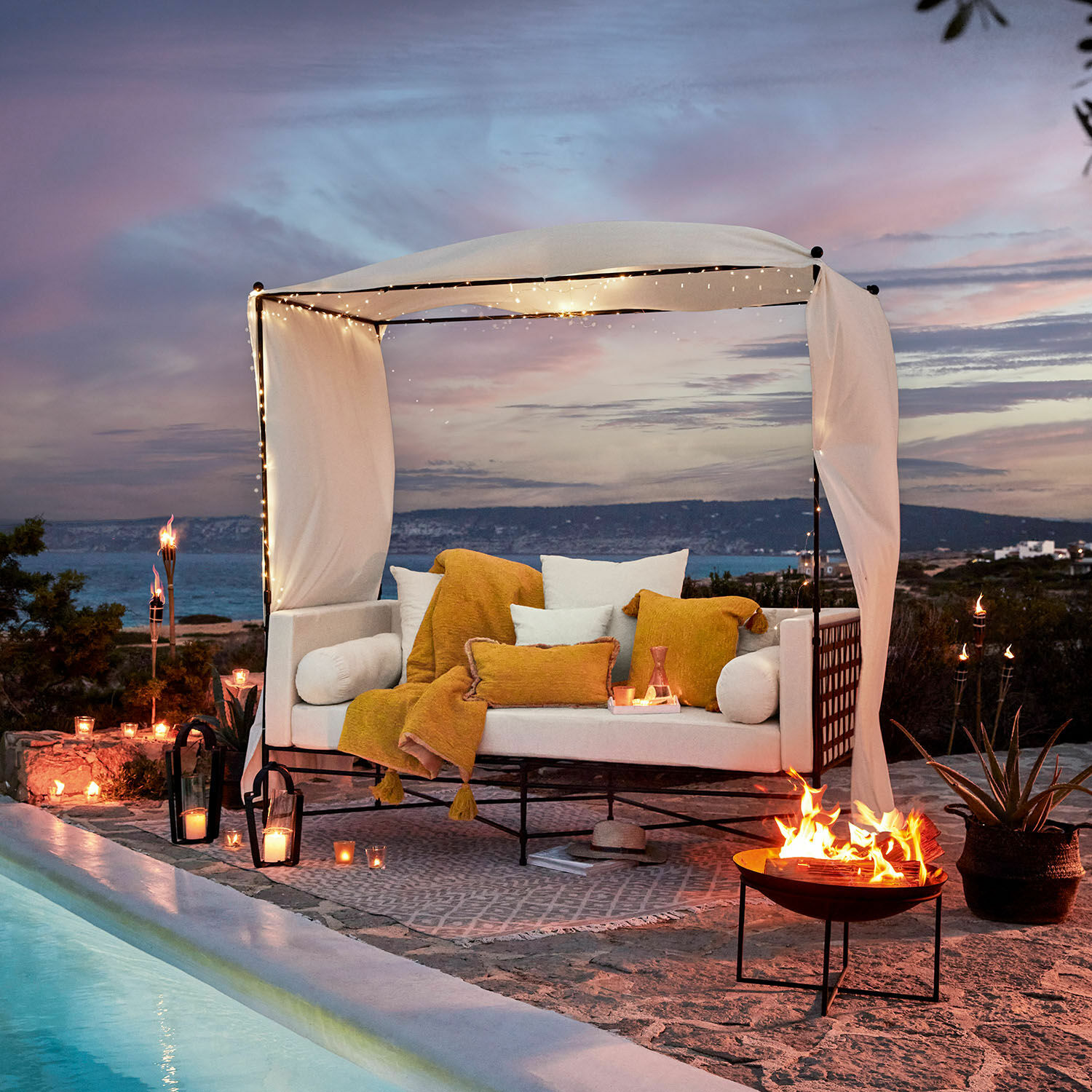 Weiße Sofa mit Metallrahmen und cremefarbenem Baldachin, gelbe Kissen, neben Pool bei Sonnenuntergang