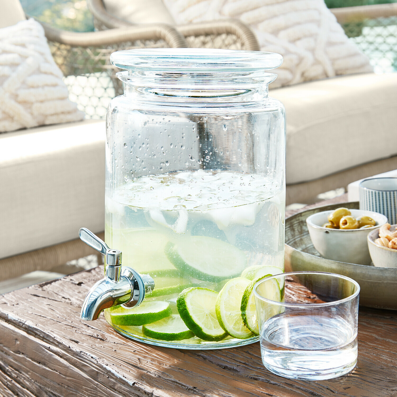 Glasgetränkespender mit Zapfhahn, gefüllt mit Wasser und Limettenscheiben auf Holztisch