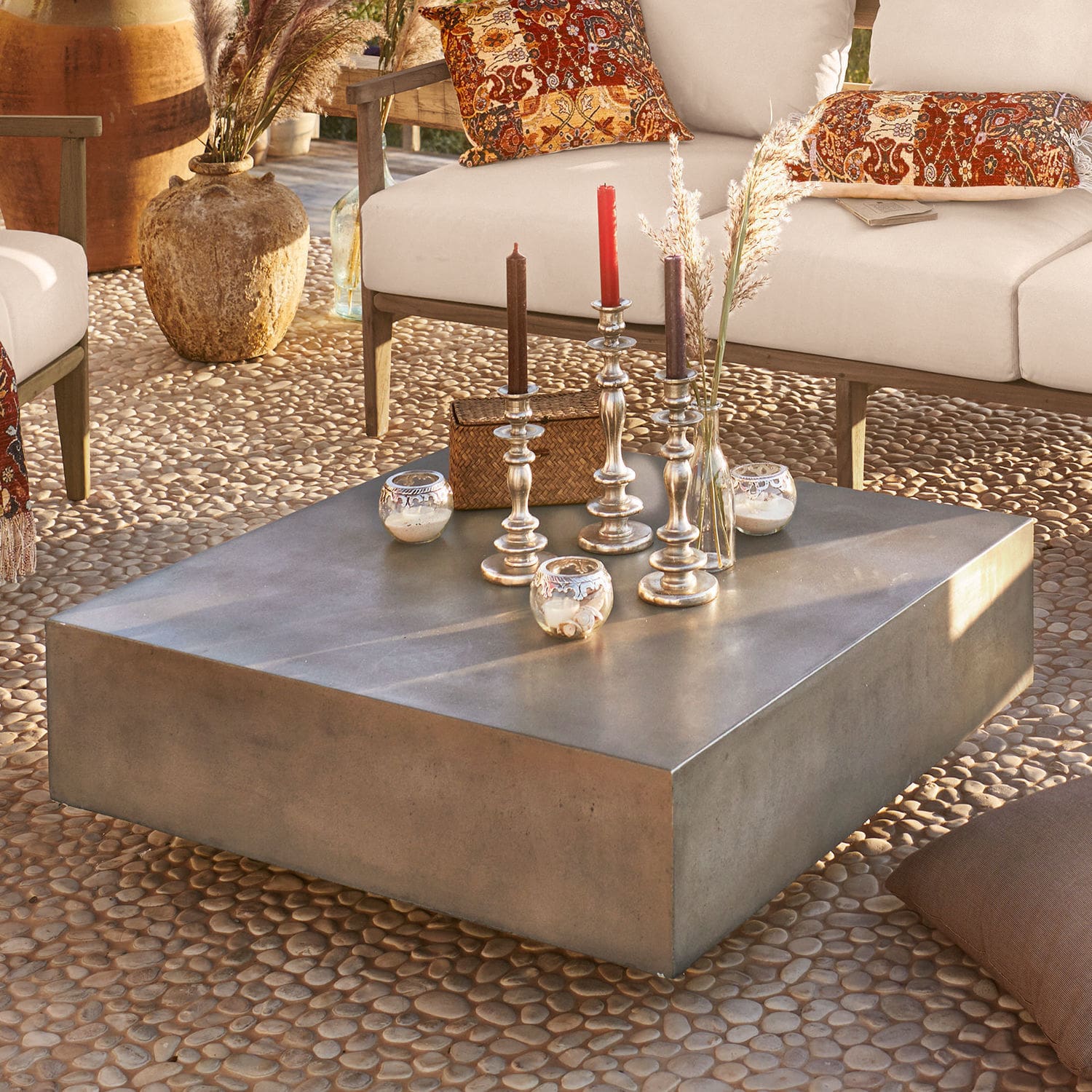 Quadratischer Couchtisch aus grauem Beton auf Terrasse mit dekorativen Kerzen und Kissen