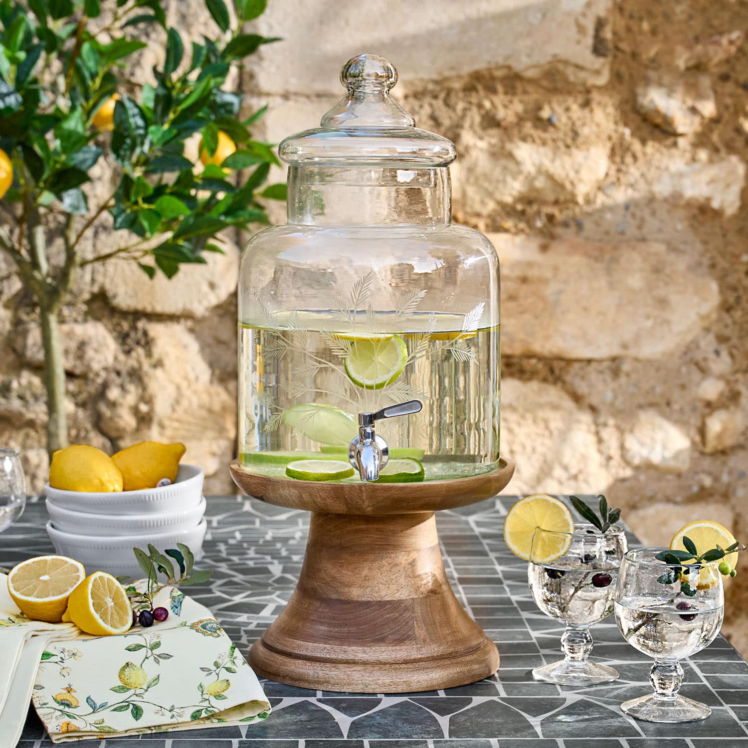 Glasgetränkespender mit Deckel auf Holzständer, Limettenscheiben und Auslaufhahn