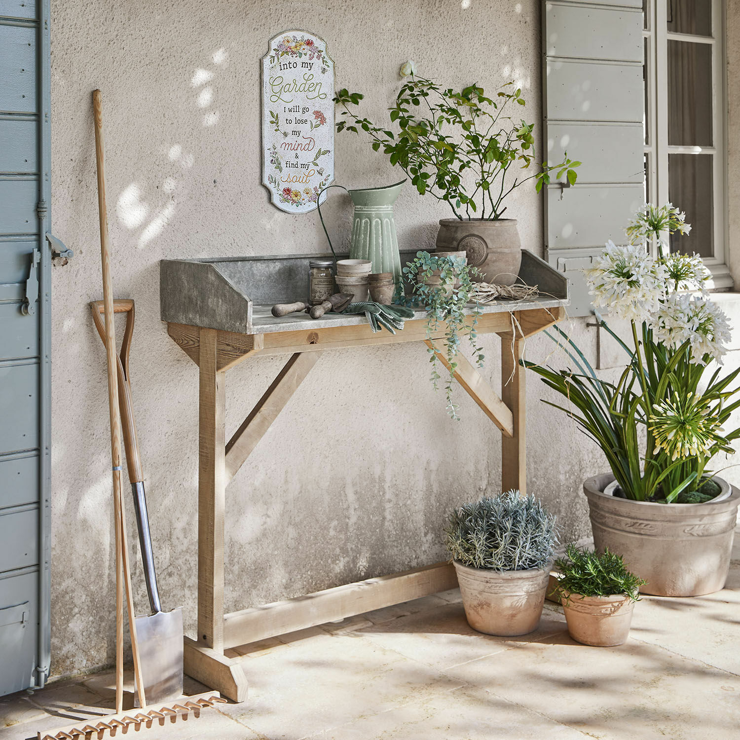 Gartentisch aus Holz mit Metallplatte, Blumentöpfe und Gartengeräte auf Terrasse, Wanddekoration