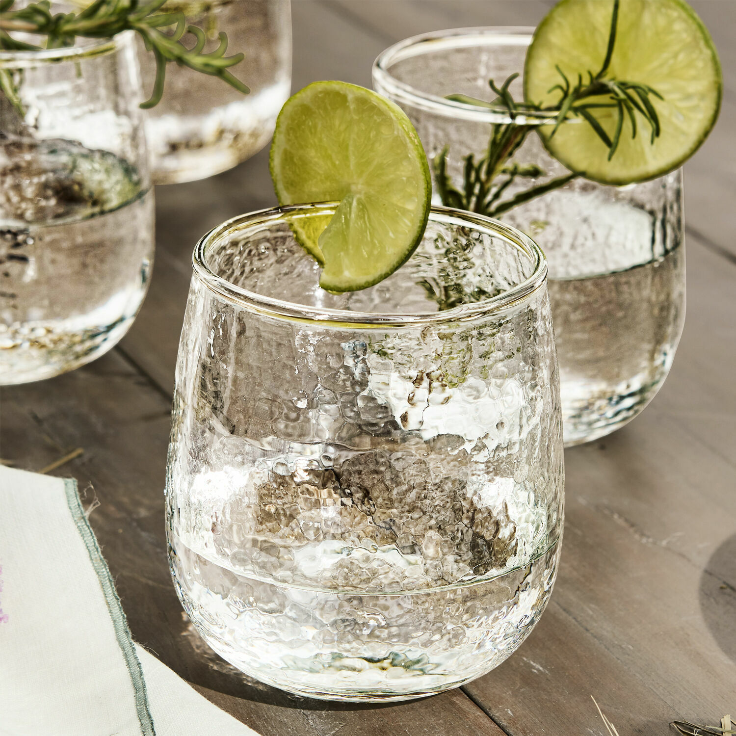 Glas aus gehämmertem Glas mit Limettenscheibe und Kräuterzweig auf Holztisch