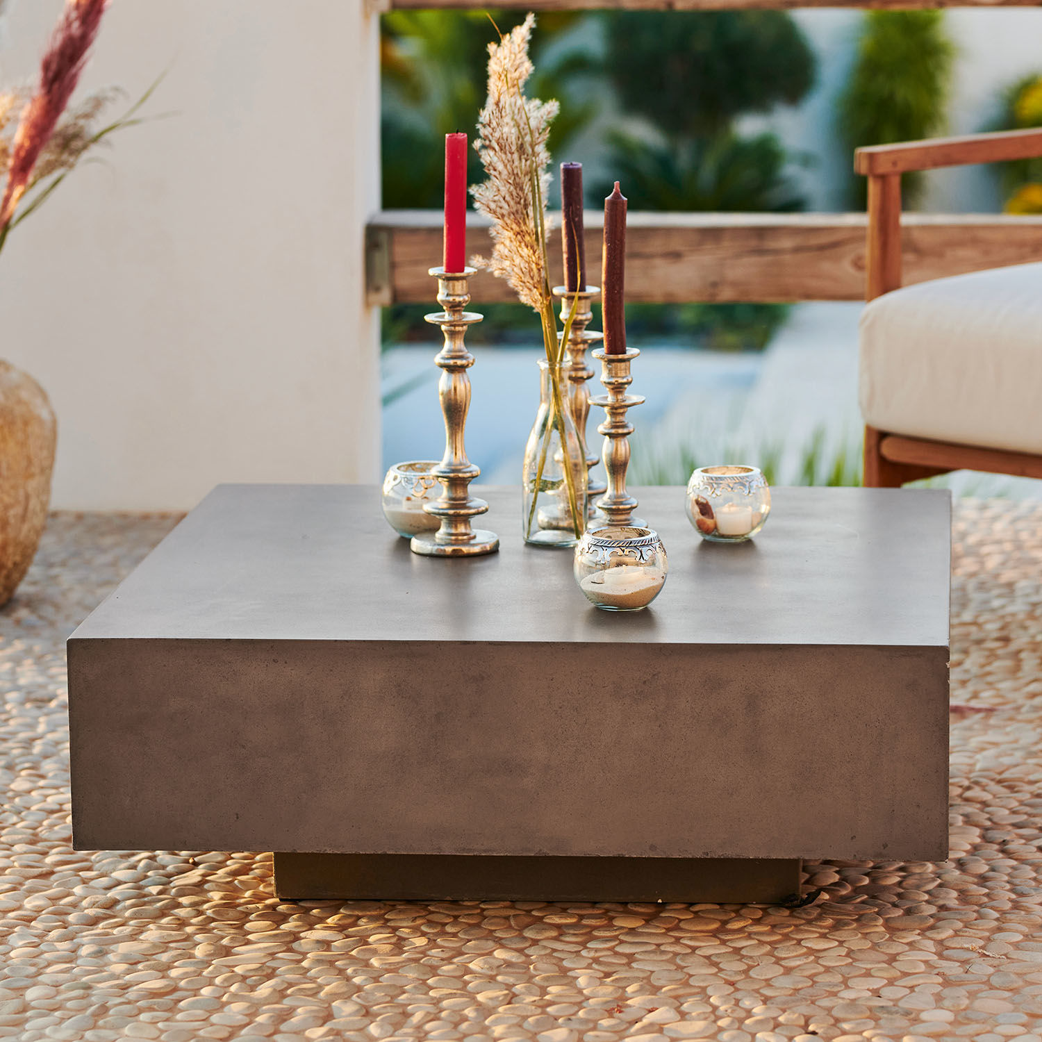 Quadratischer Couchtisch aus grauem Beton mit dekorativen Kerzen und Vase auf Terrasse