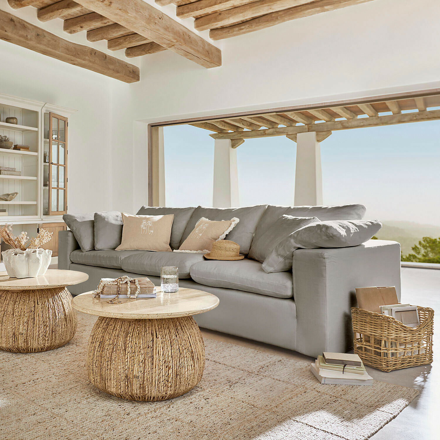 Graues Sofa mit weichen Kissen und natürlichen Holzcouchtischen in hellem Wohnzimmer mit Aussicht