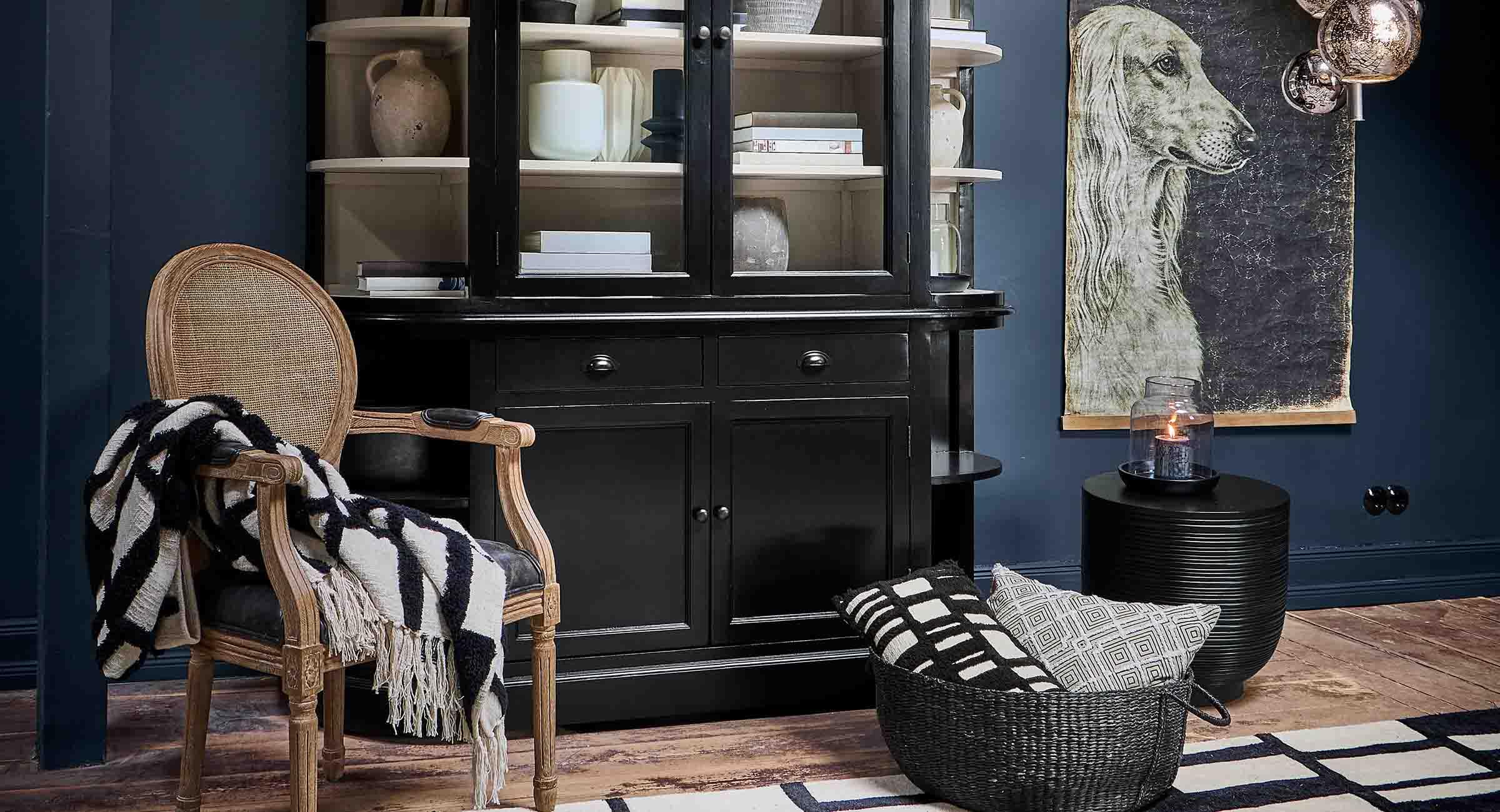Schwarze Holzvitrine mit Regalen, Naturdekorationen und Korbsessel in stilvollem Wohnzimmer