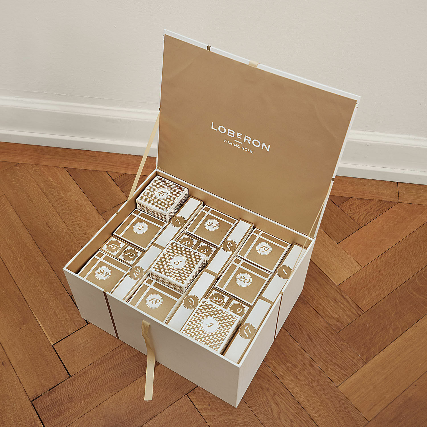 Eleganter Adventskalender aus Karton in Beige und Weiß mit nummerierten Schachteln auf Holzparkett
