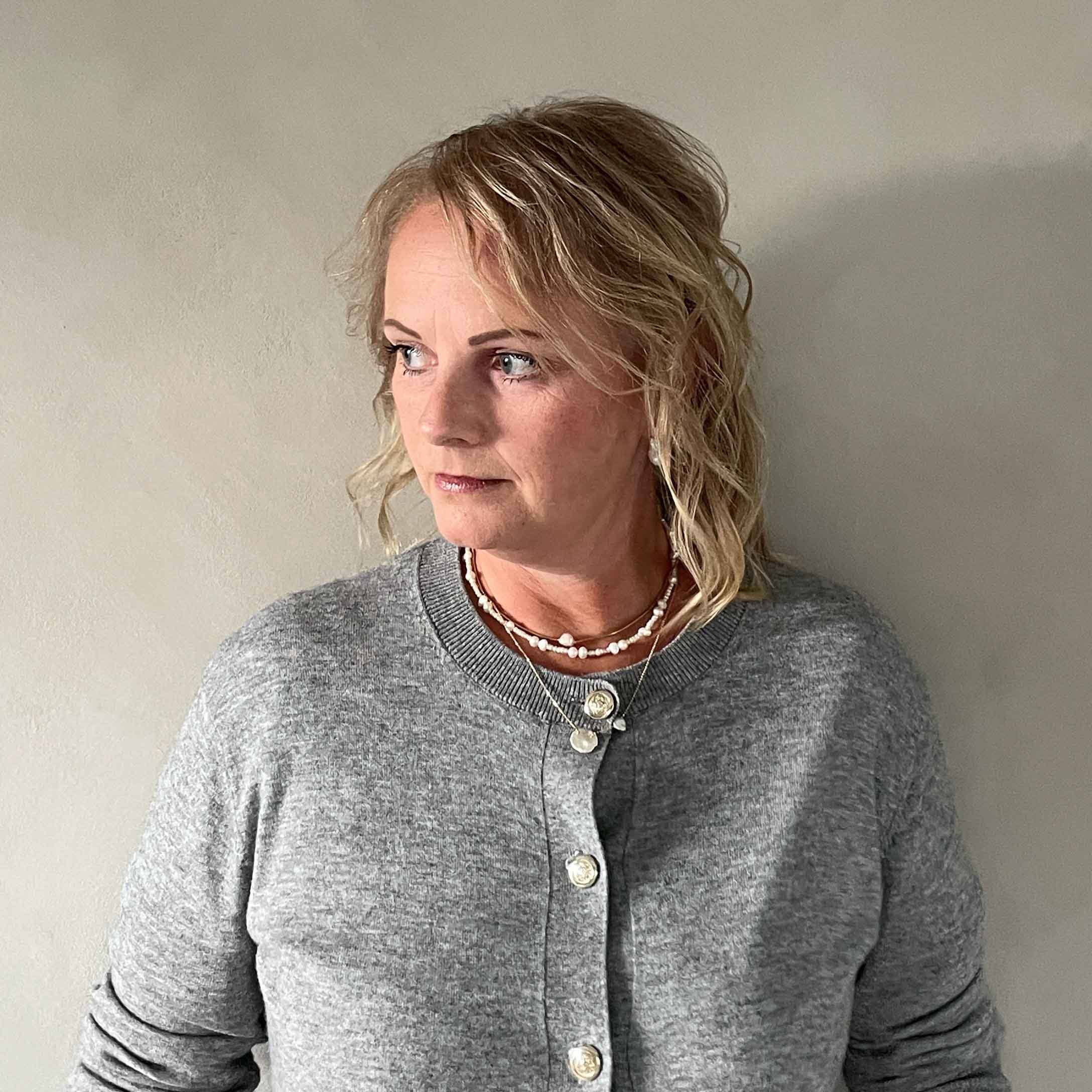 Frau in grauem Strickjacke mit Knöpfen und Halsketten vor hellem Hintergrund, Casual-Look