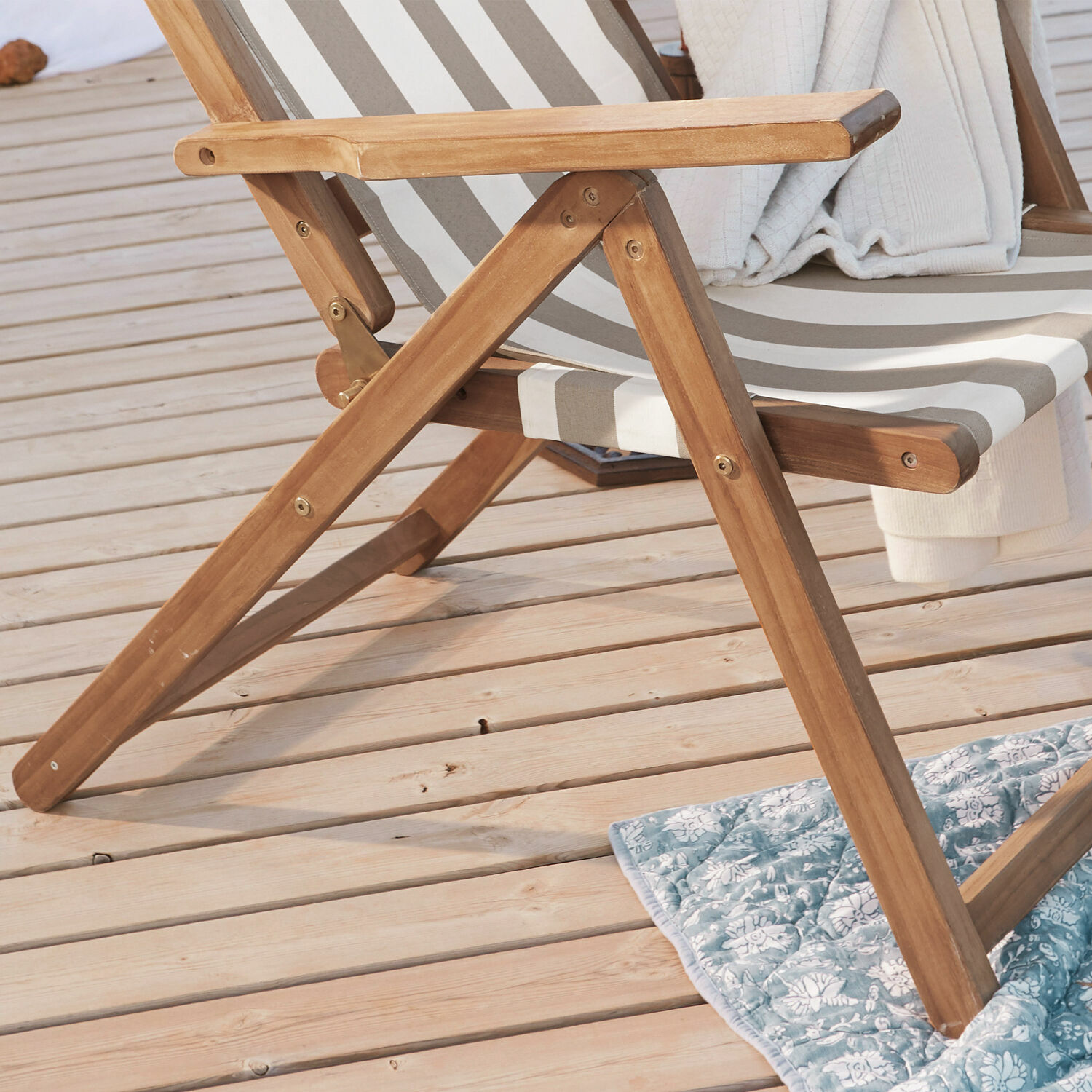 Liegestuhl aus Holz mit beige-weiß gestreiftem Stoff auf Holzterrasse mit Kissen