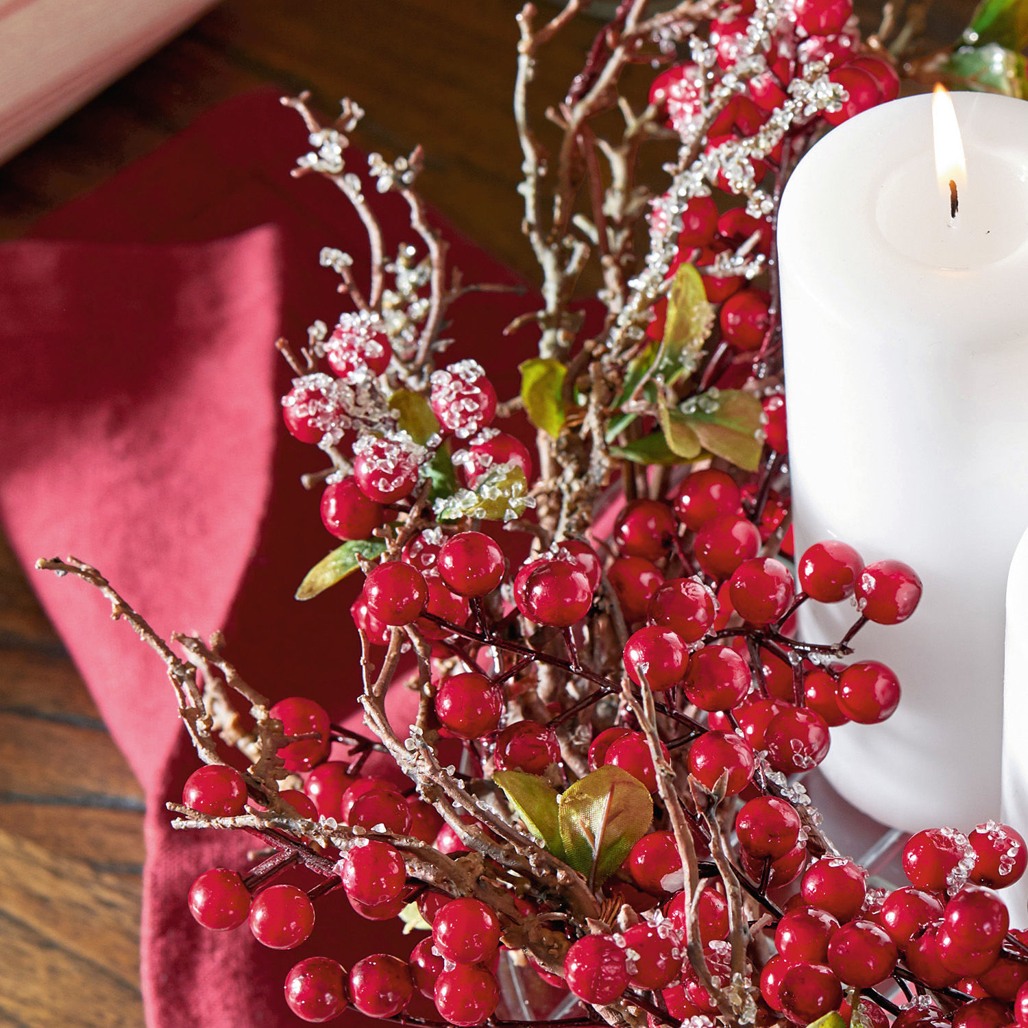 Dekoration mit roten Beeren und Zweigen mit weißen Kristallen neben weißer Kerze auf rotem Hintergrund