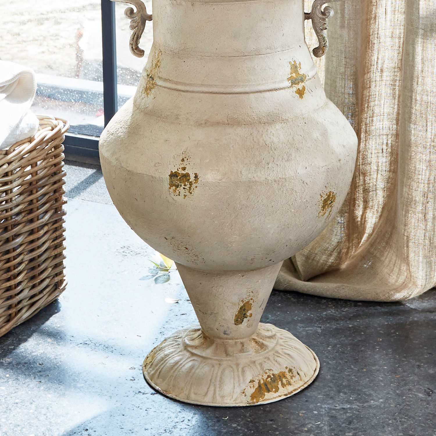 Große dekorative Vase aus gealtertem beigem Metall auf Boden in hellem Raum