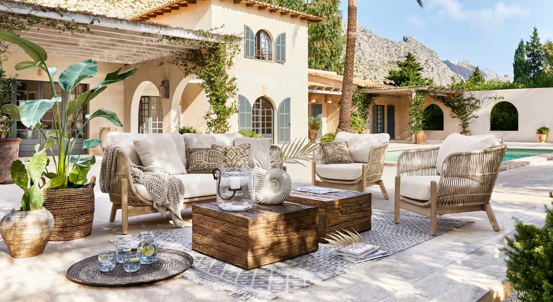 Gartenmöbel-Set mit hellen Polstern und Holztisch auf Terrasse neben Pool im mediterranen Stil