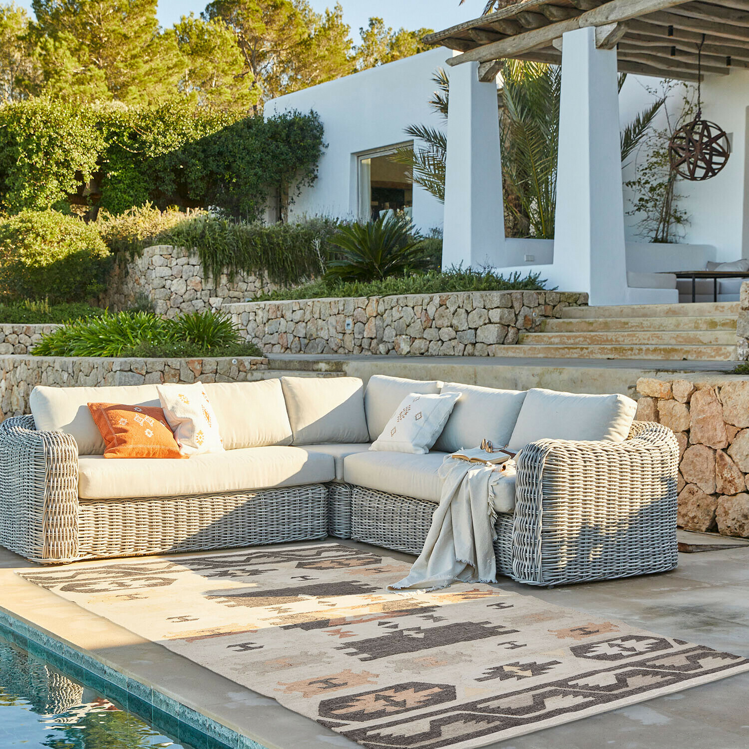 Eck-Gartensofa aus grauem Rattan mit hellen Polstern neben dem Pool