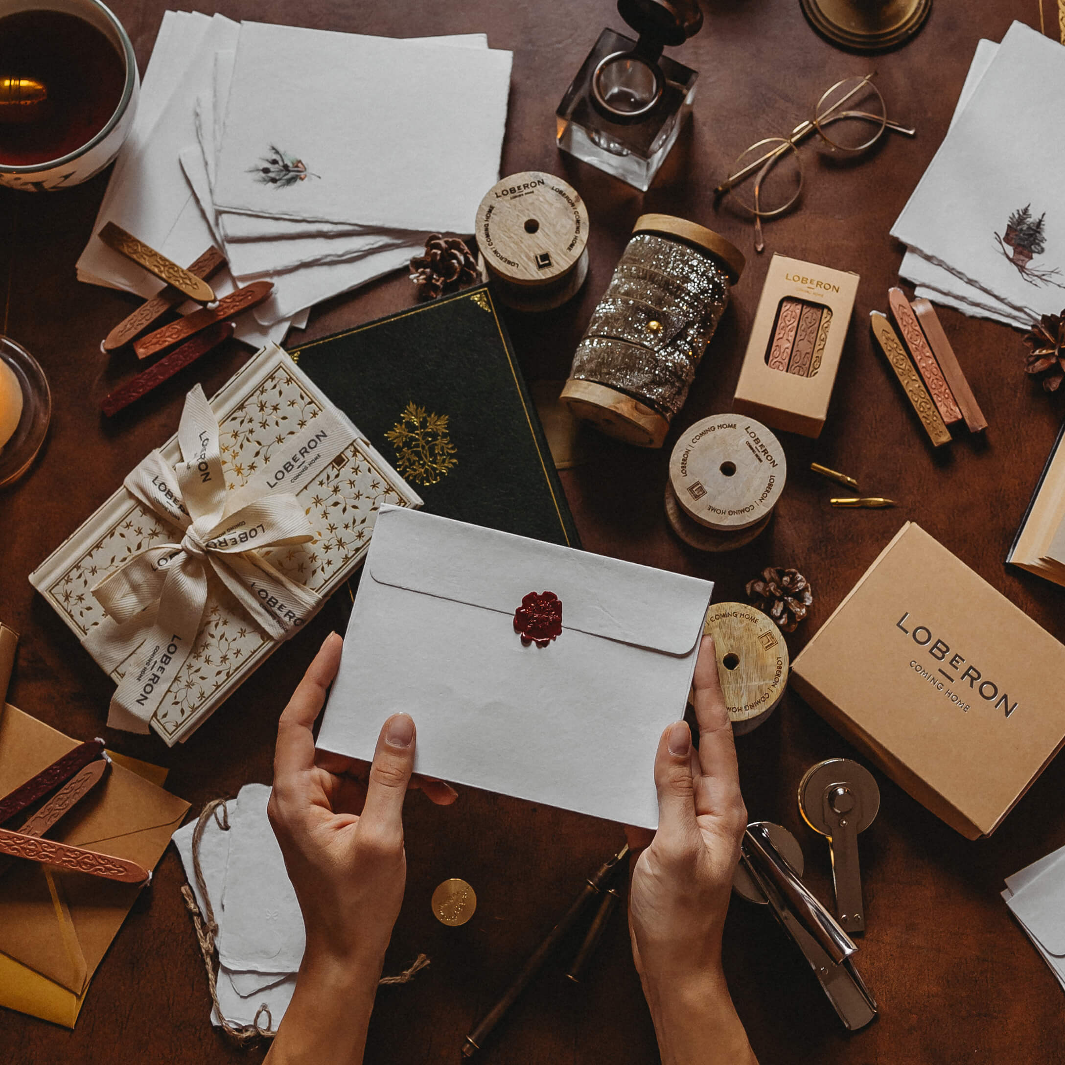 Hände halten weißen Umschlag mit rotem Siegel umgeben von Loberon Schreib- und Dekorationsmaterialien.