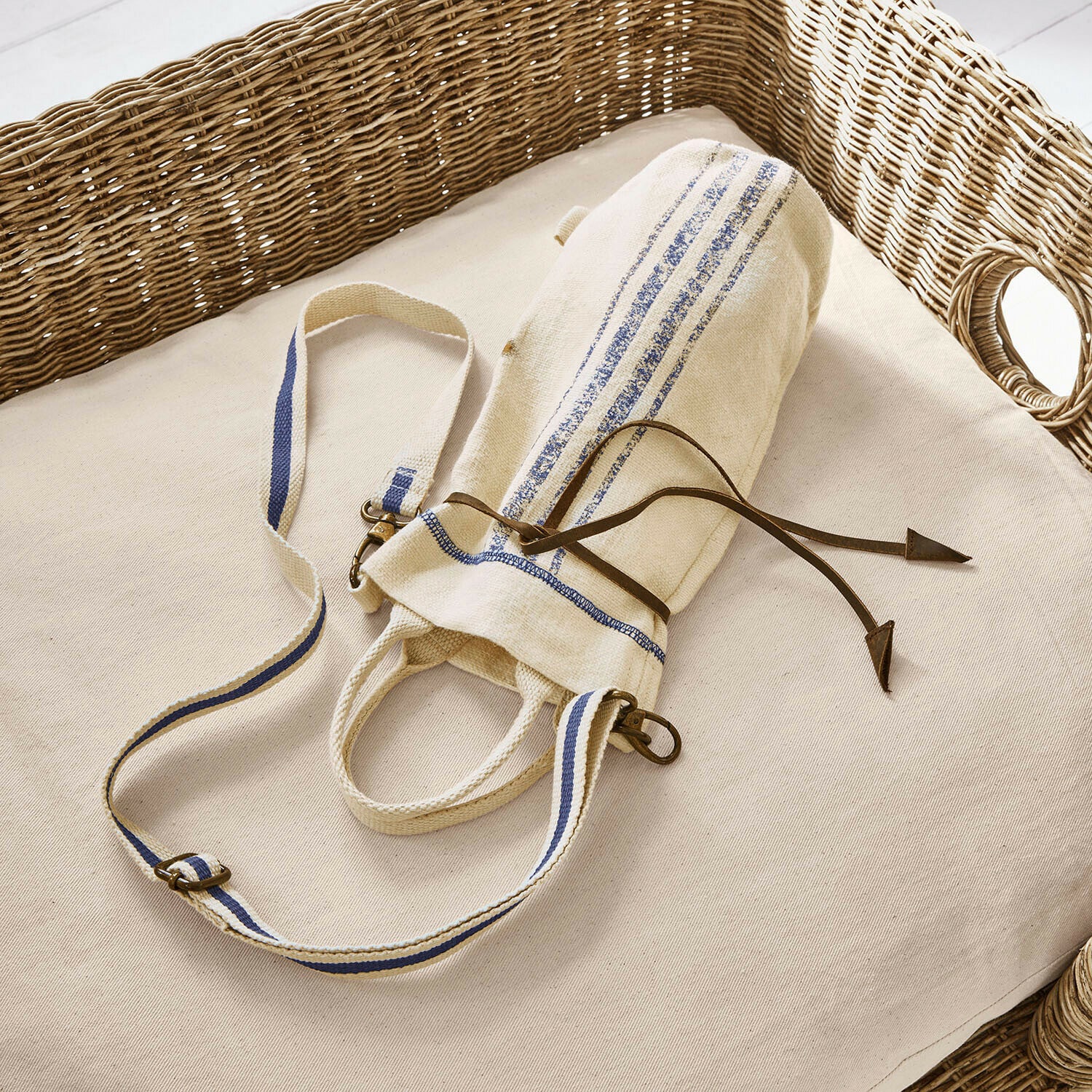 Flaschentragetasche Pawera Beige Baumwolltasche mit blauen Streifen und Lederkordel auf hellem Kissen mit Korbgeflecht