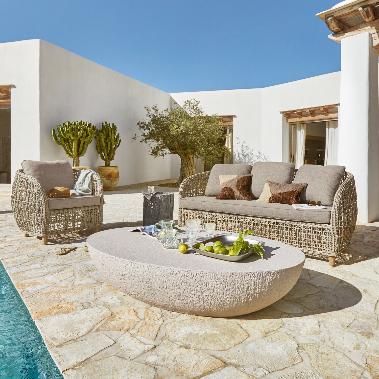 Gartenmöbel-Set aus beigem Rattan mit Polstern und steinernem Tisch auf Terrasse am Pool