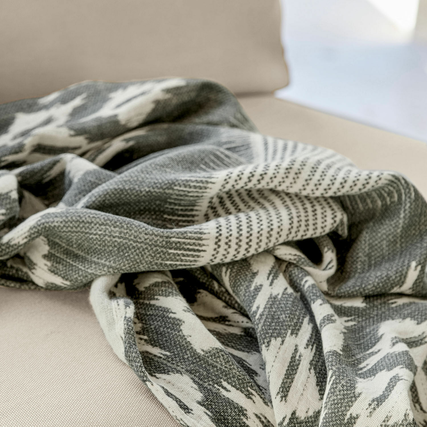 Grau-weiß gemusterte Decke aus weichem Material auf beigem Sofa, Wohnaccessoire