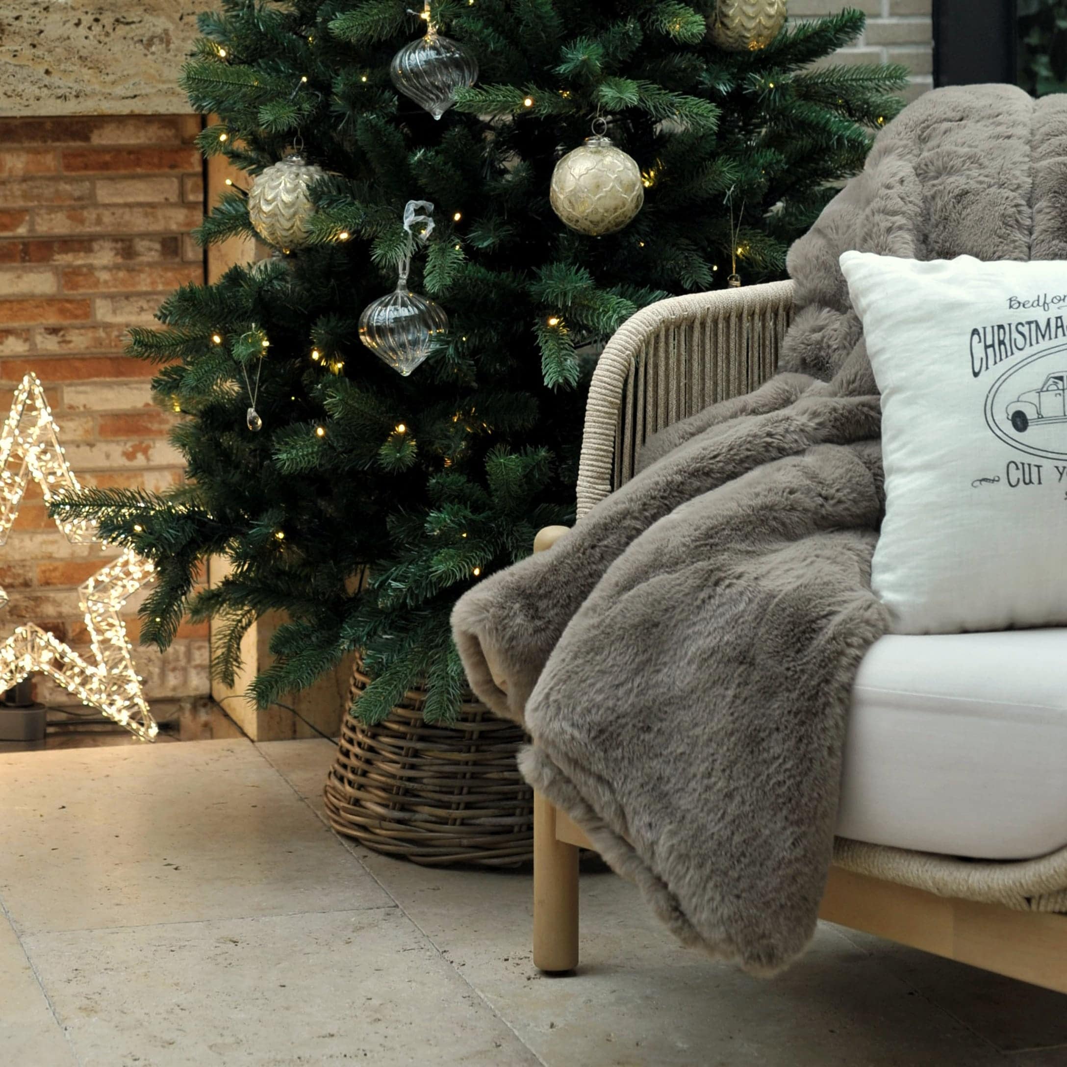 Weicher grauer Kunstfellplaid auf Stuhl neben geschmücktem Weihnachtsbaum und leuchtendem Stern