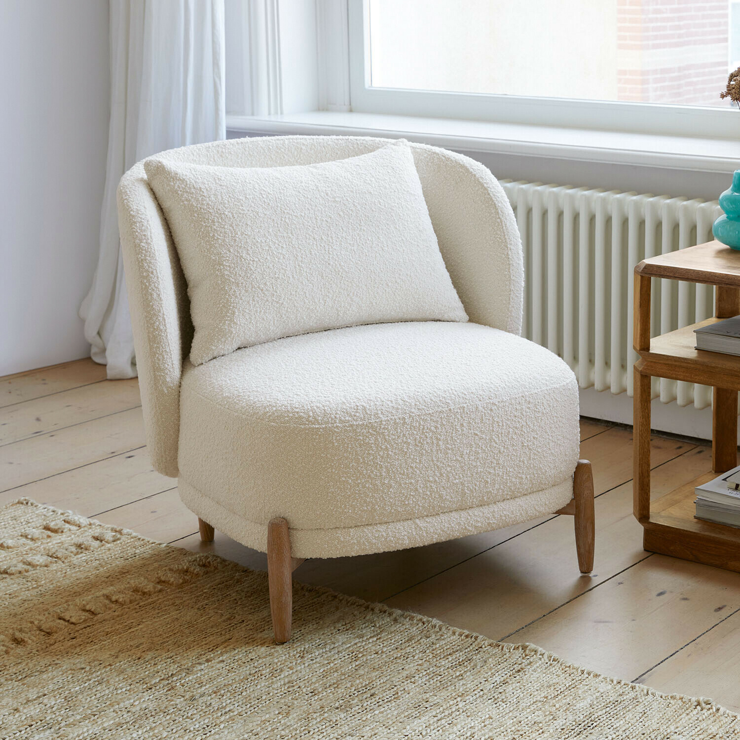 Weißer Sessel aus weichem Bouclé-Stoff mit Holzbeinen in hellem Wohnzimmer