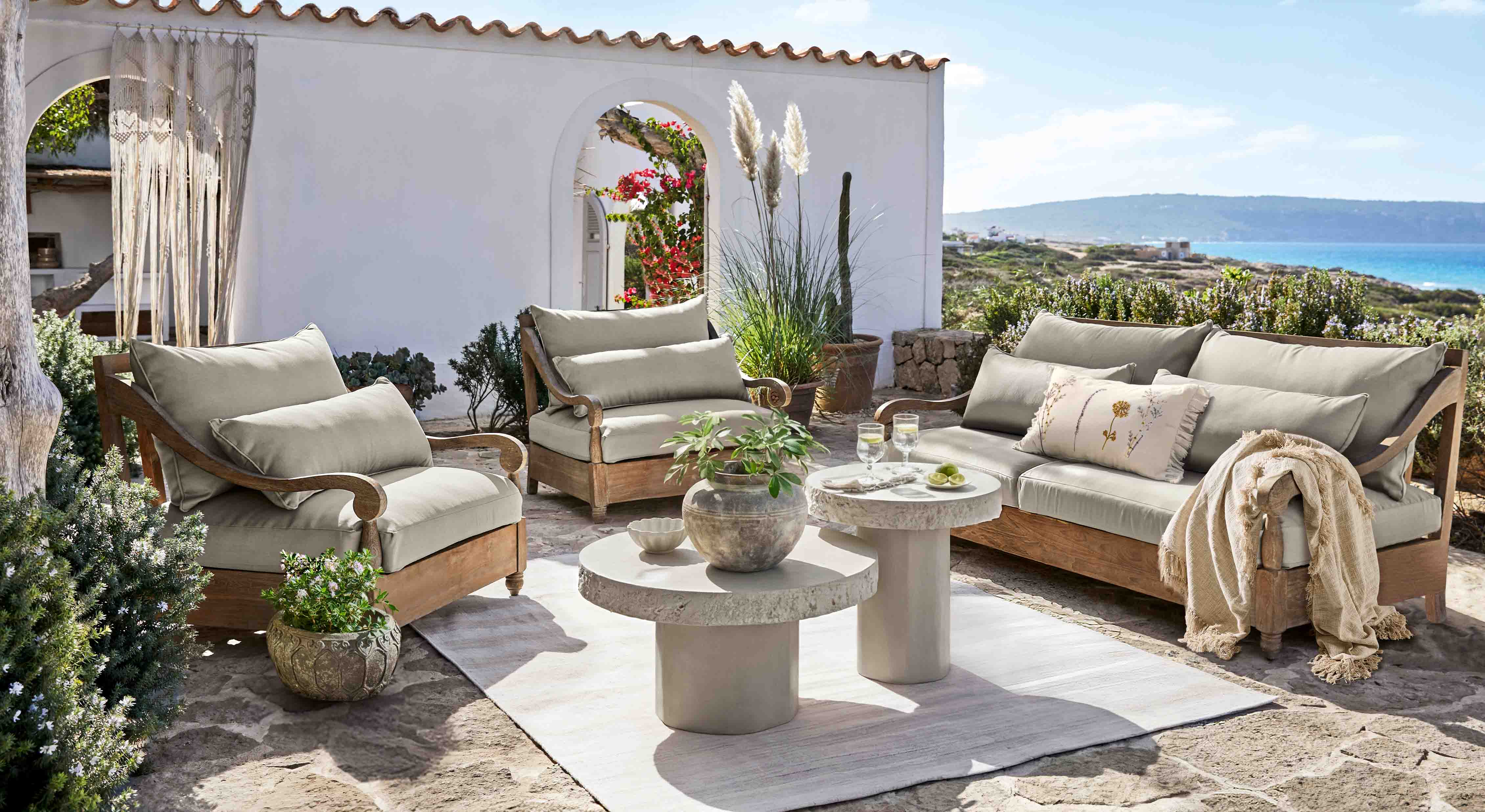 Gartenmöbel-Set aus Holz mit grauen Polstern auf Terrasse mit Meerblick