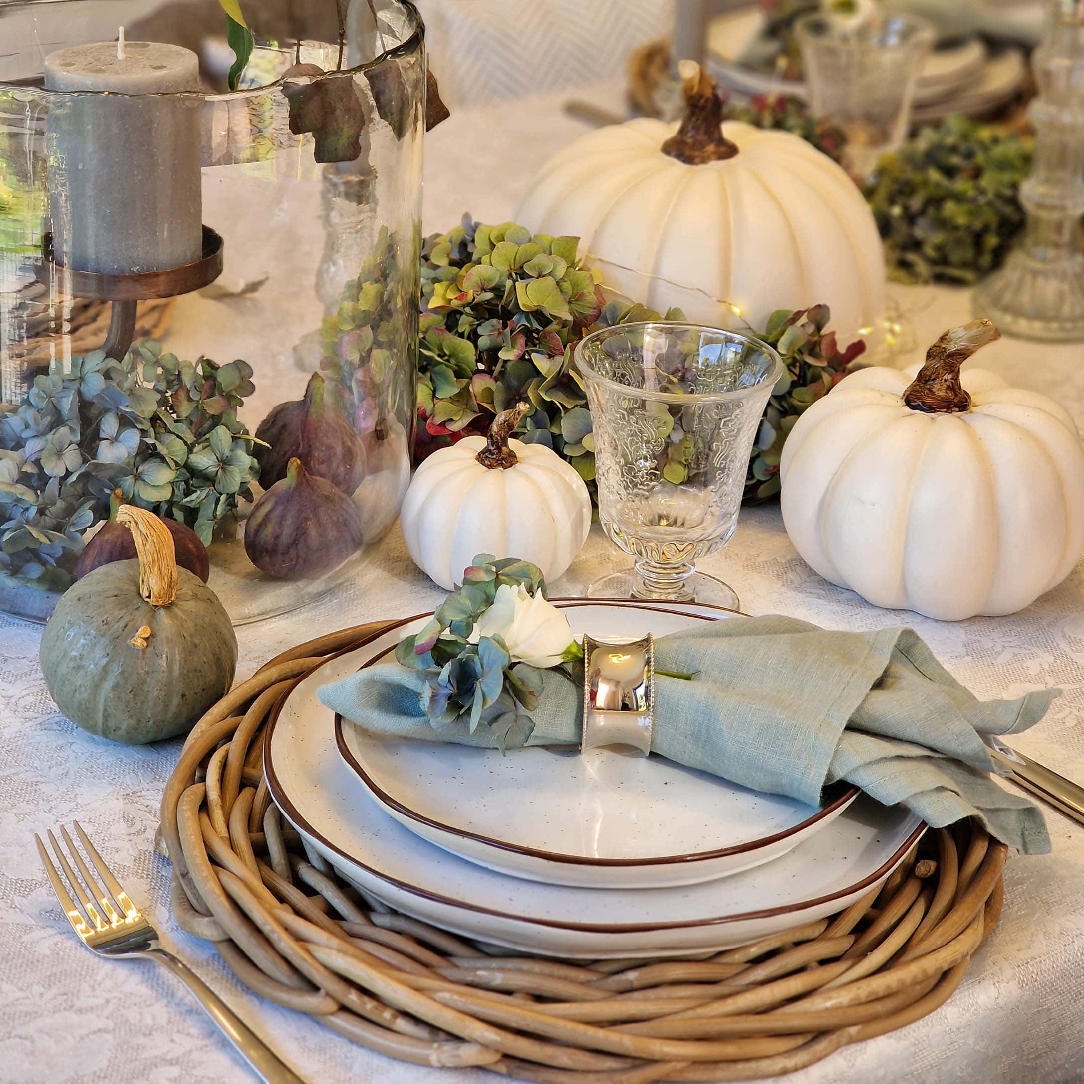 Tischdekoration mit weißen und grünen Kürbissen, Glas und Leinenserviette auf Keramiktellern