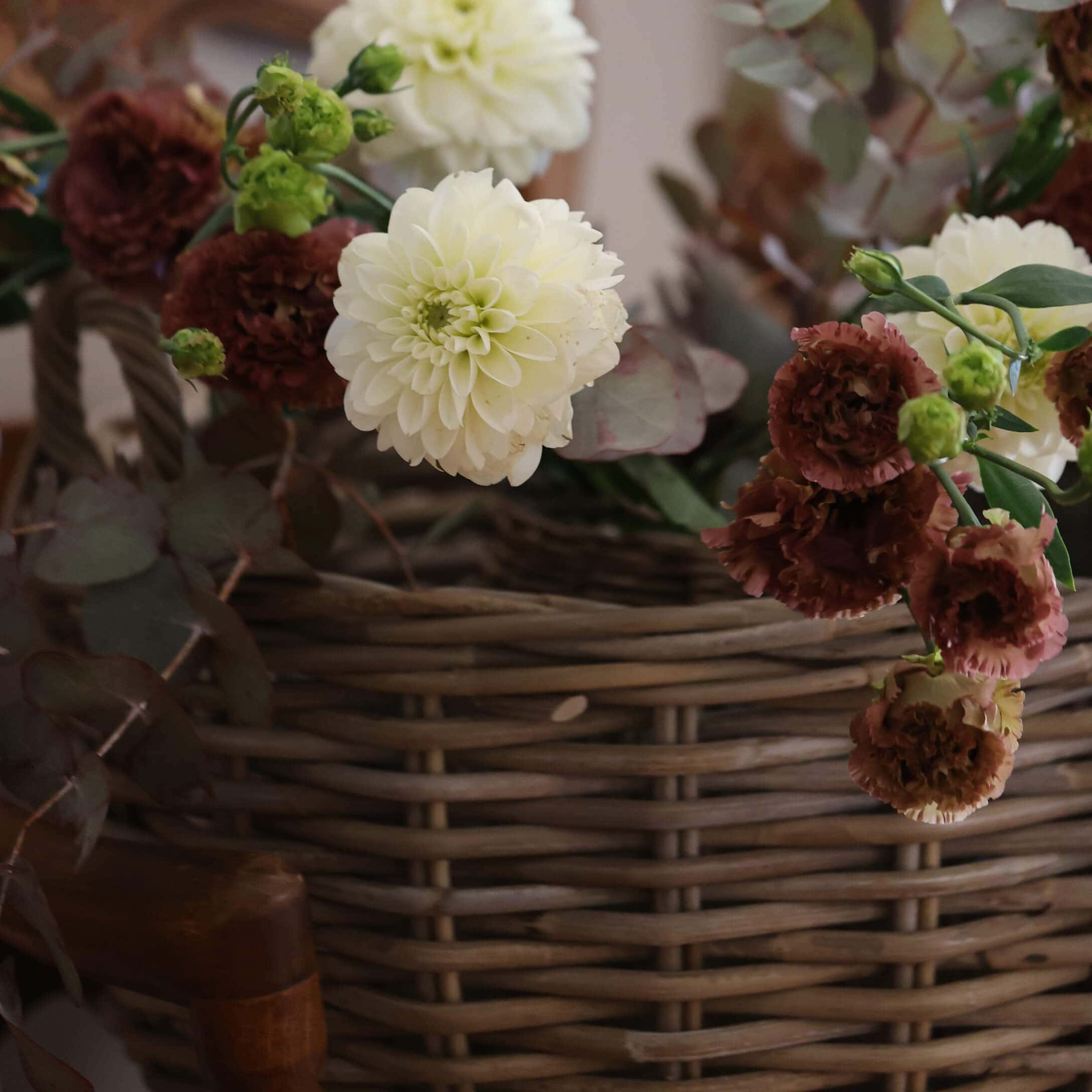 Strauß aus cremefarbenen und bordeauxroten Blumen in einem Weidenkorb als Wohnaccessoire