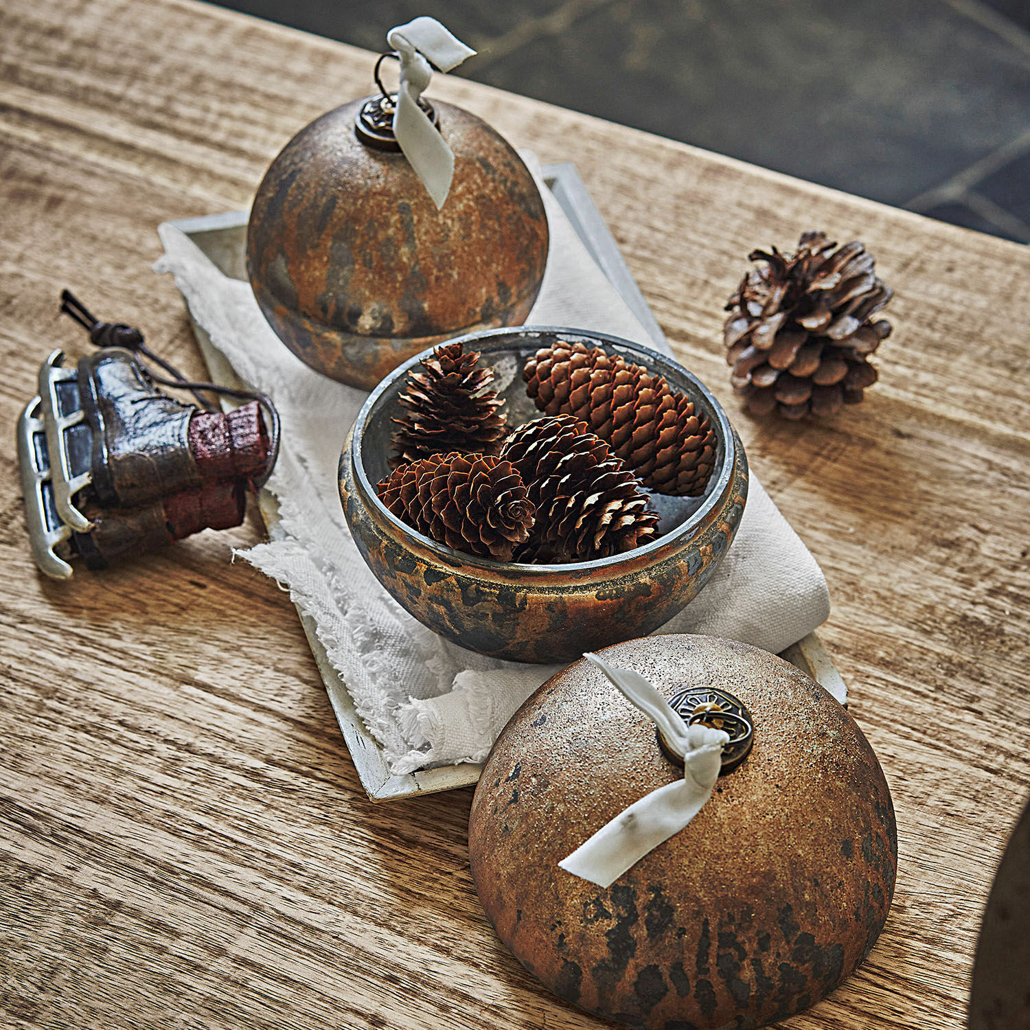 Dekorative Metallkugel in Rostoptik mit Tannenzapfen auf Holztisch, rustikale Weihnachtsdeko
